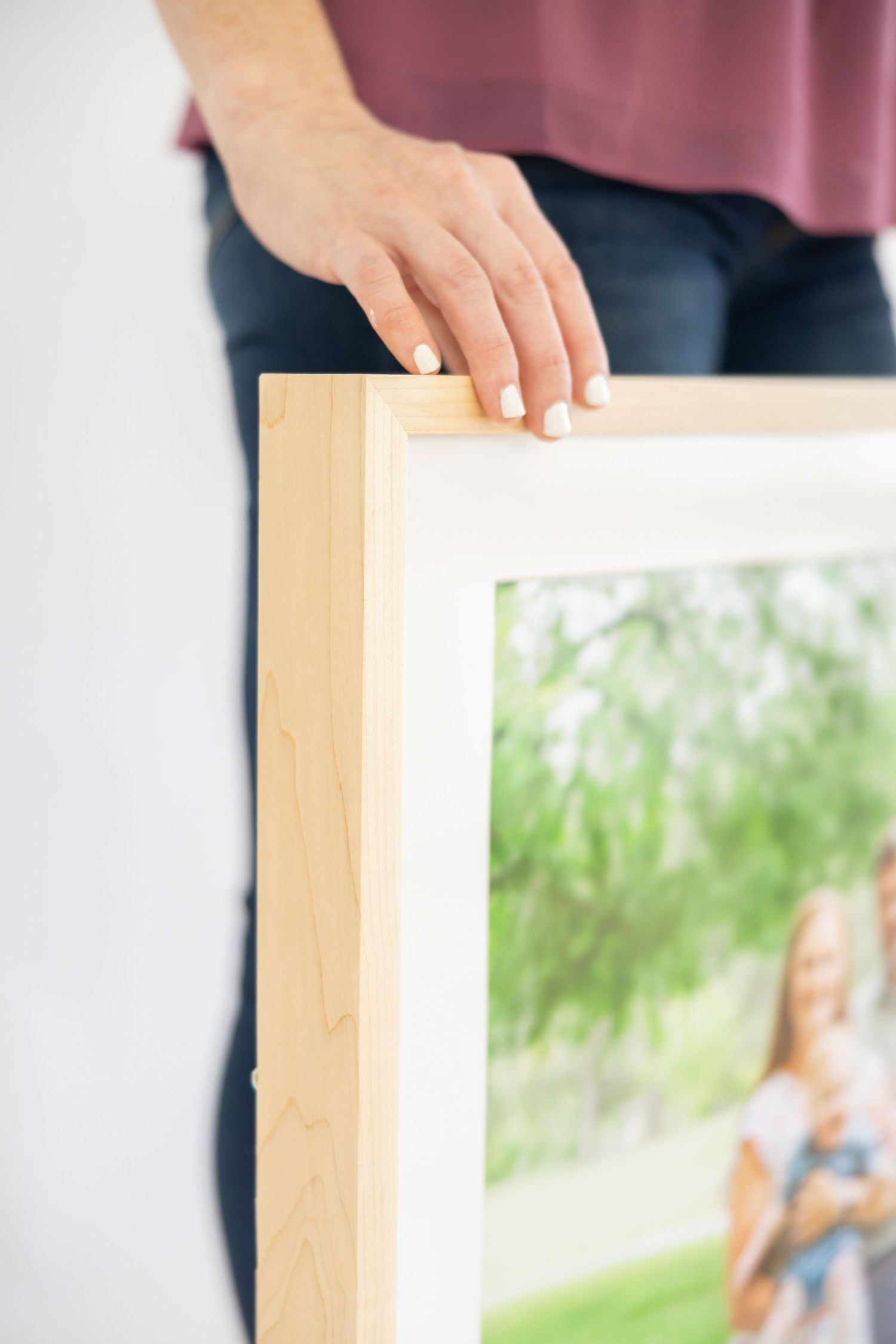 Hands holding a wooden frame against a blurred background with greenery and natural light.