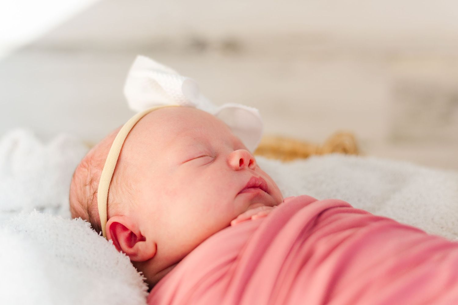 Peaceful newborn sleeping soundly while wearing pink clothing and resting on soft white blankets.