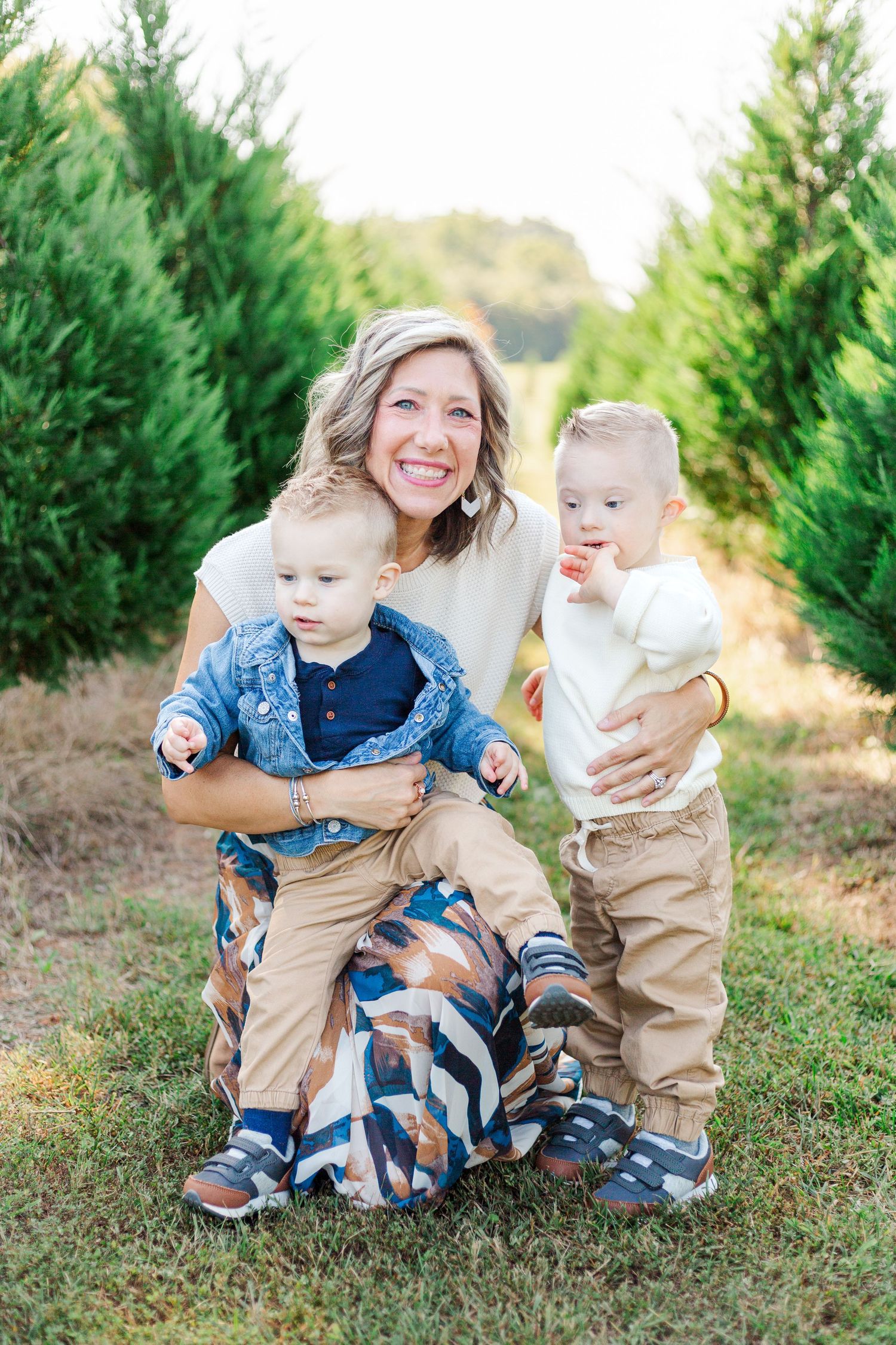 A family sitting together among evergreen trees in for a Christmas tree farm photoshoot in Greenville, SC