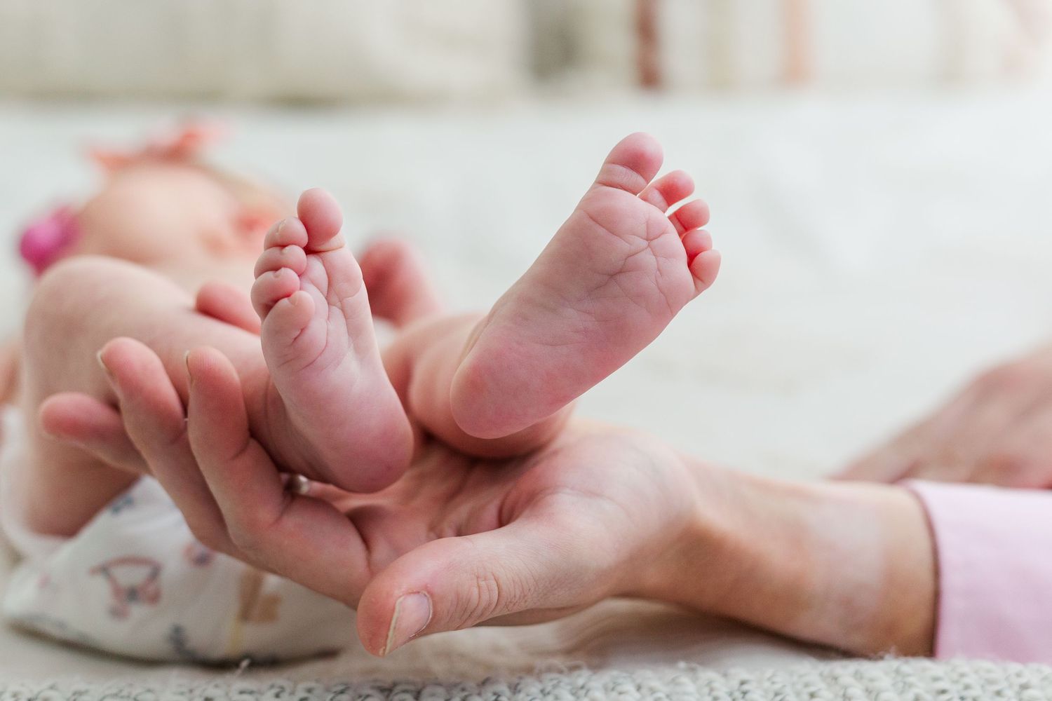 Close-up of a parent gently holding a newborn baby's tiny feet in their hands.