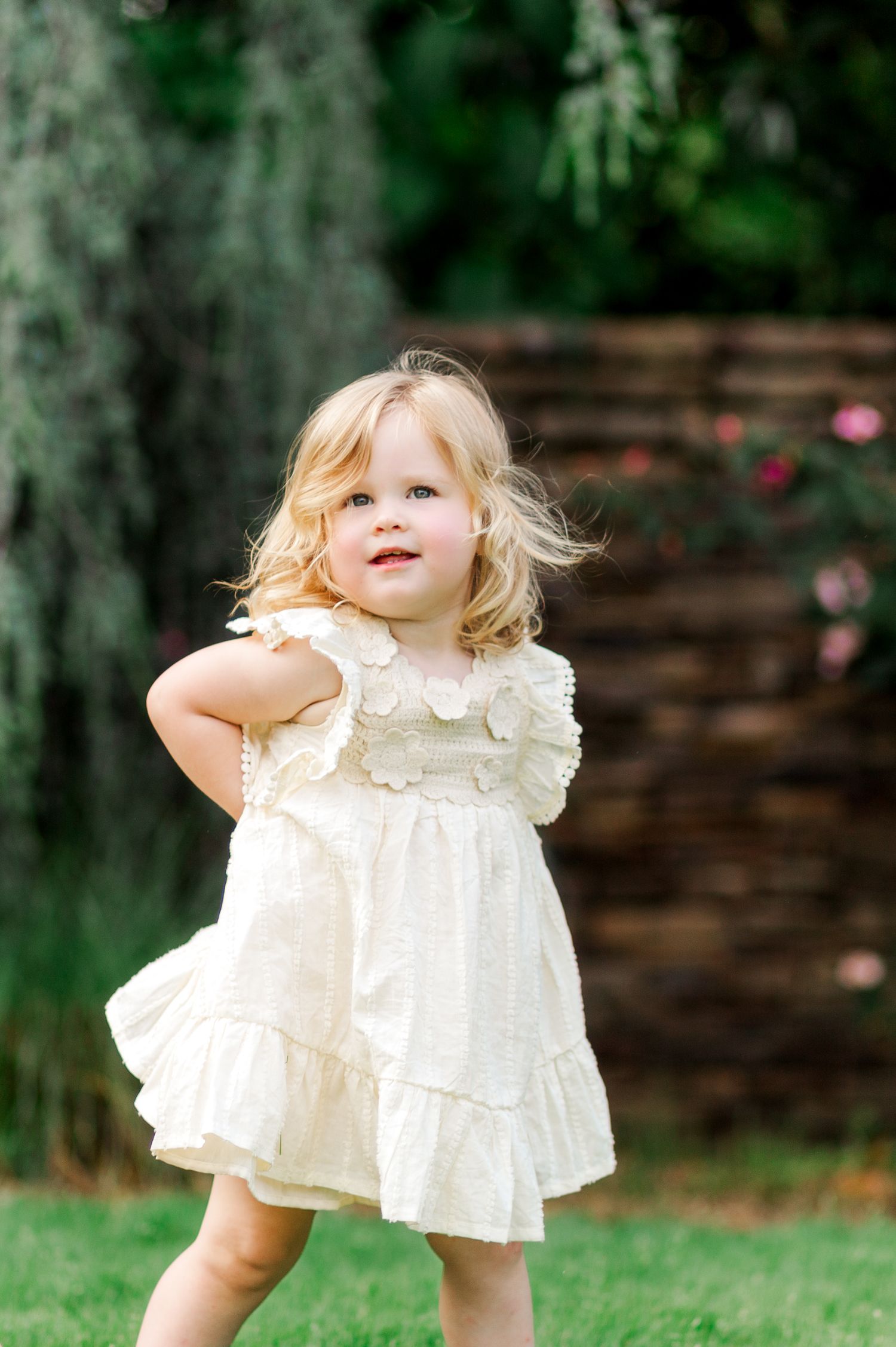 Toddler in Clemson, SC in white ruffled dress playing outdoors on green grass for a family photo session.
