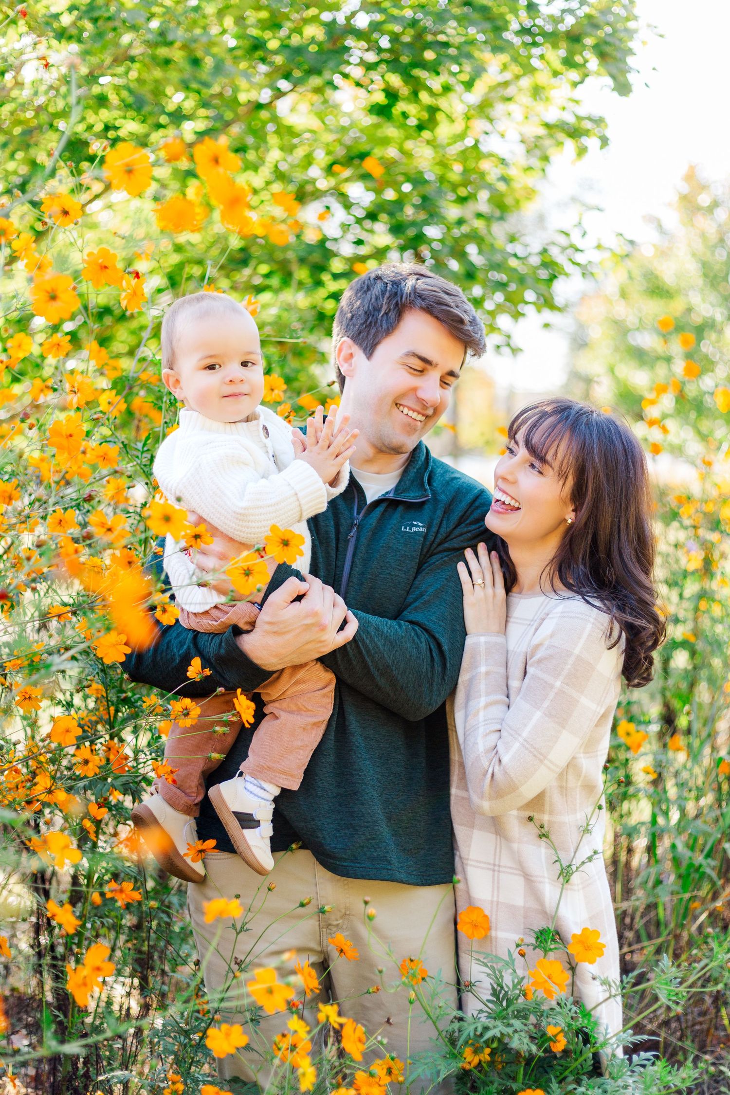 A family shares a joyful moment together surrounded by blooming orange cosmos flowers in a garden setting.