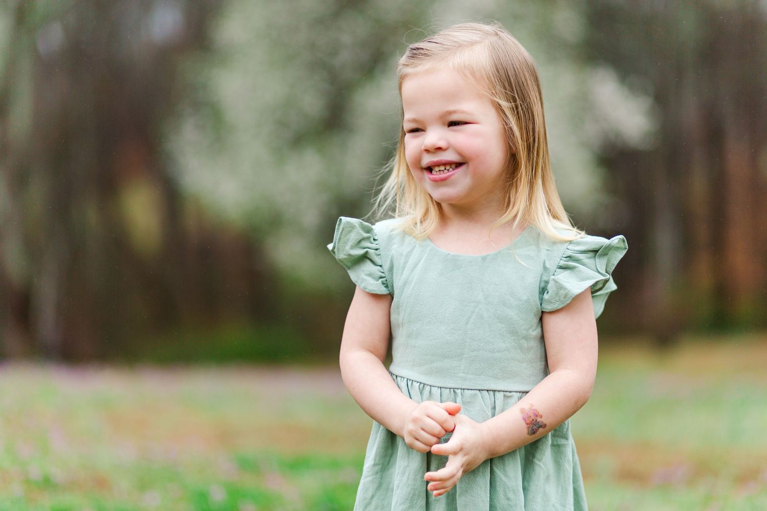 A small child in a mint green dress smiling in a forest setting.