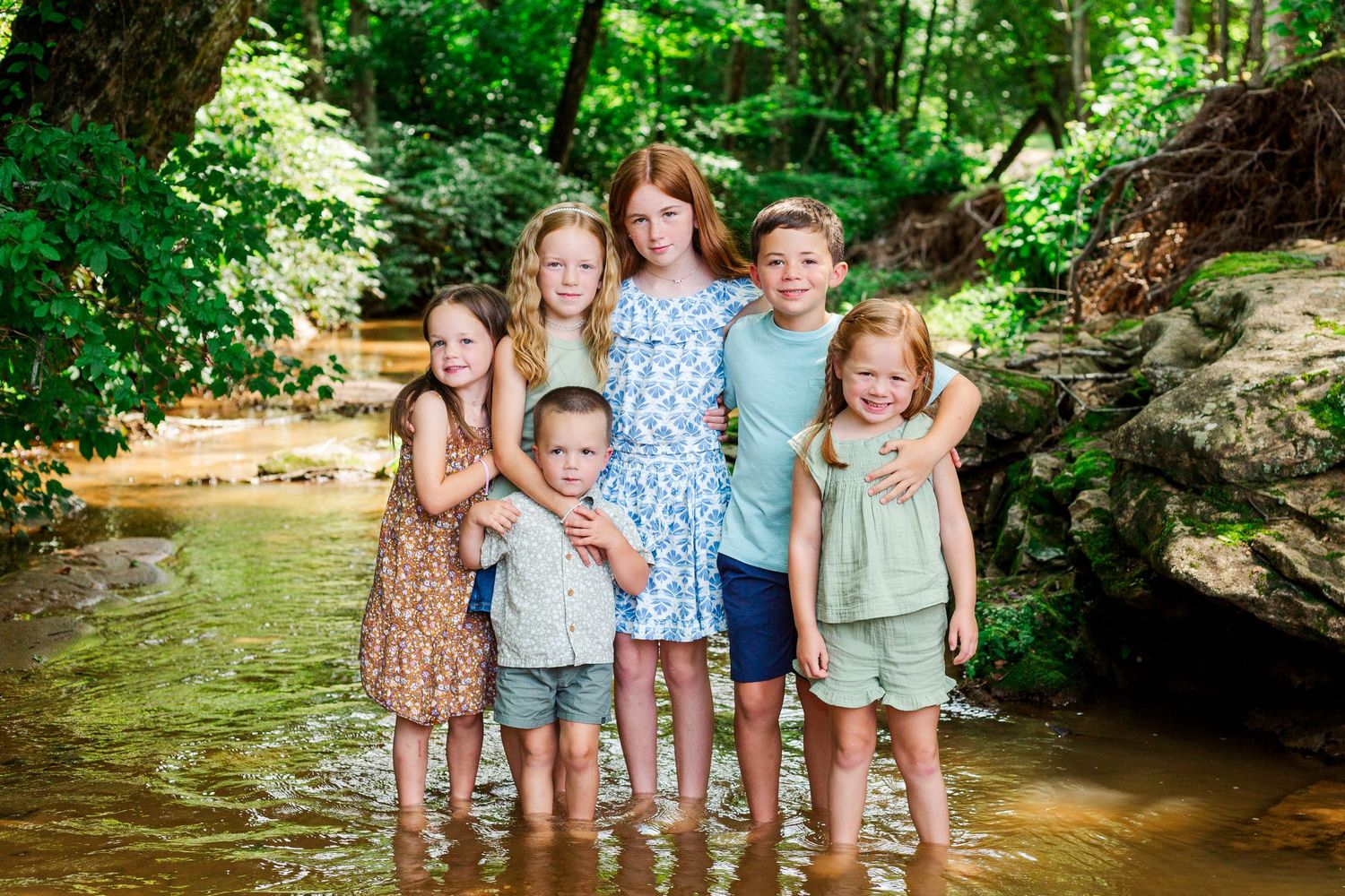 Multiple generations gather in a creek bed surrounded by dense forest for summer photos.