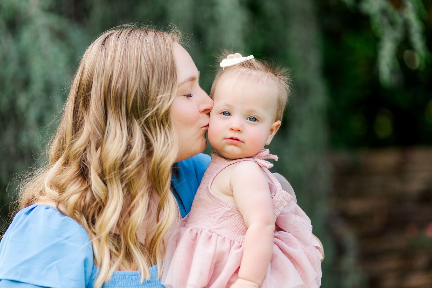 A tender moment captured in Clemson, SC as a woman in blue kisses a baby wearing a pink dress for a family photo session.