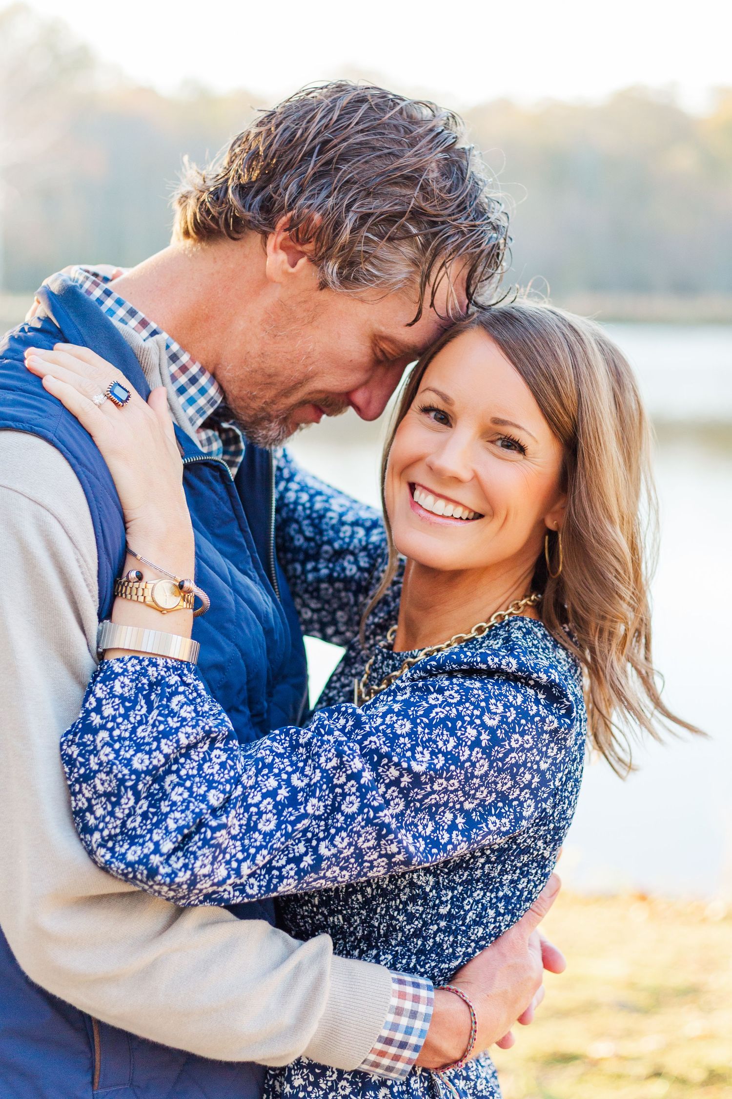A couple embraces lovingly during a sunset photoshoot by the water wearing coordinating blue outfits.