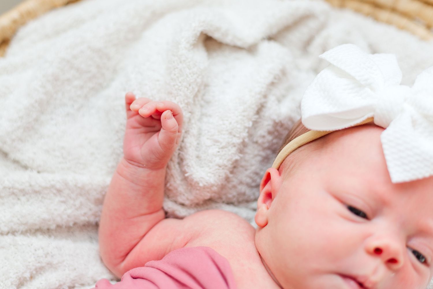 Sleeping baby in pink clothing lying on white blanket with a white bow headband.