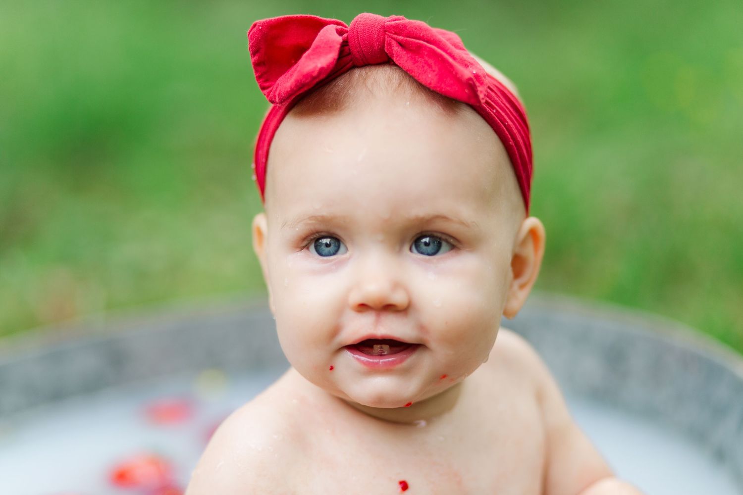 A child wearing a red headband bow sits outdoors in Greenville, SC for a milestone session
