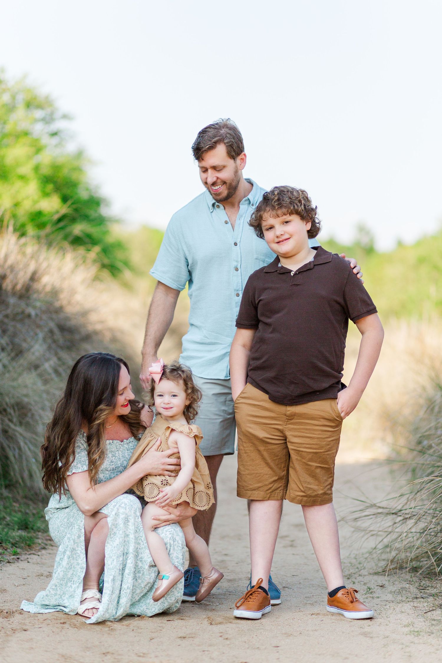 Family enjoying a tender moment together on a sandy beach path during an outdoor photo session.