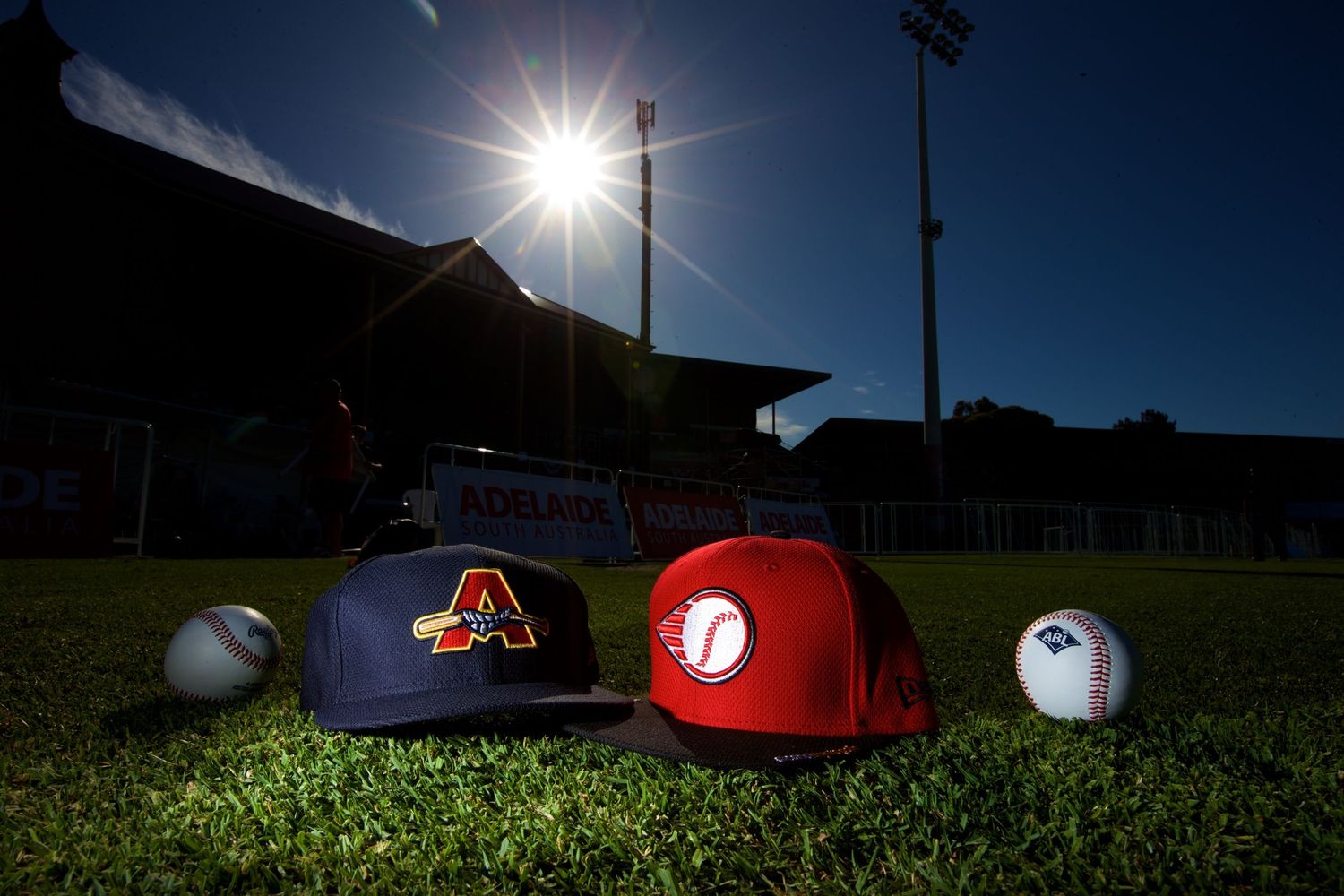 Baseball caps and equipment laid out on grass field under bright sunlight.