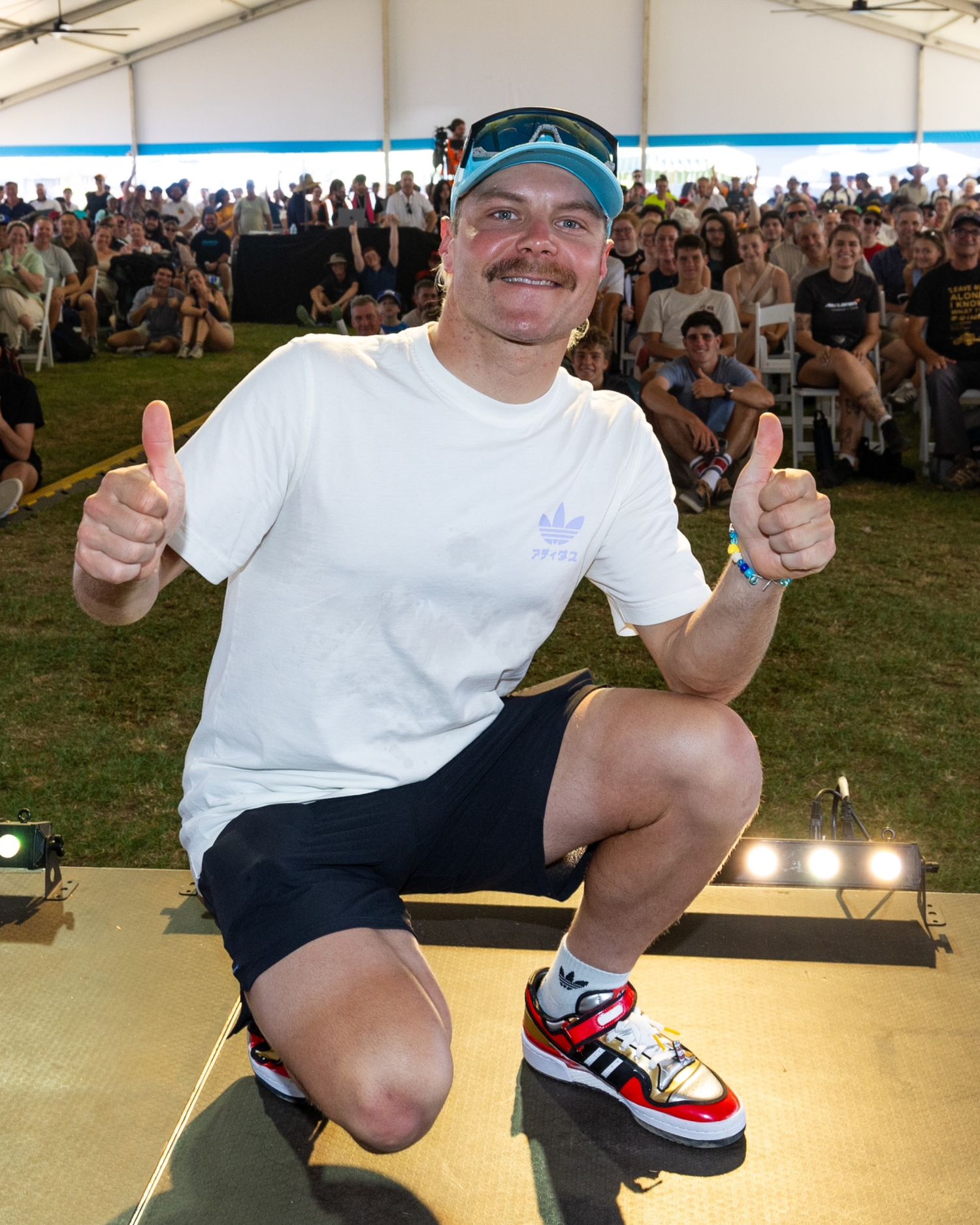 Person in white t-shirt and shorts performs skateboarding tricks on a stage.