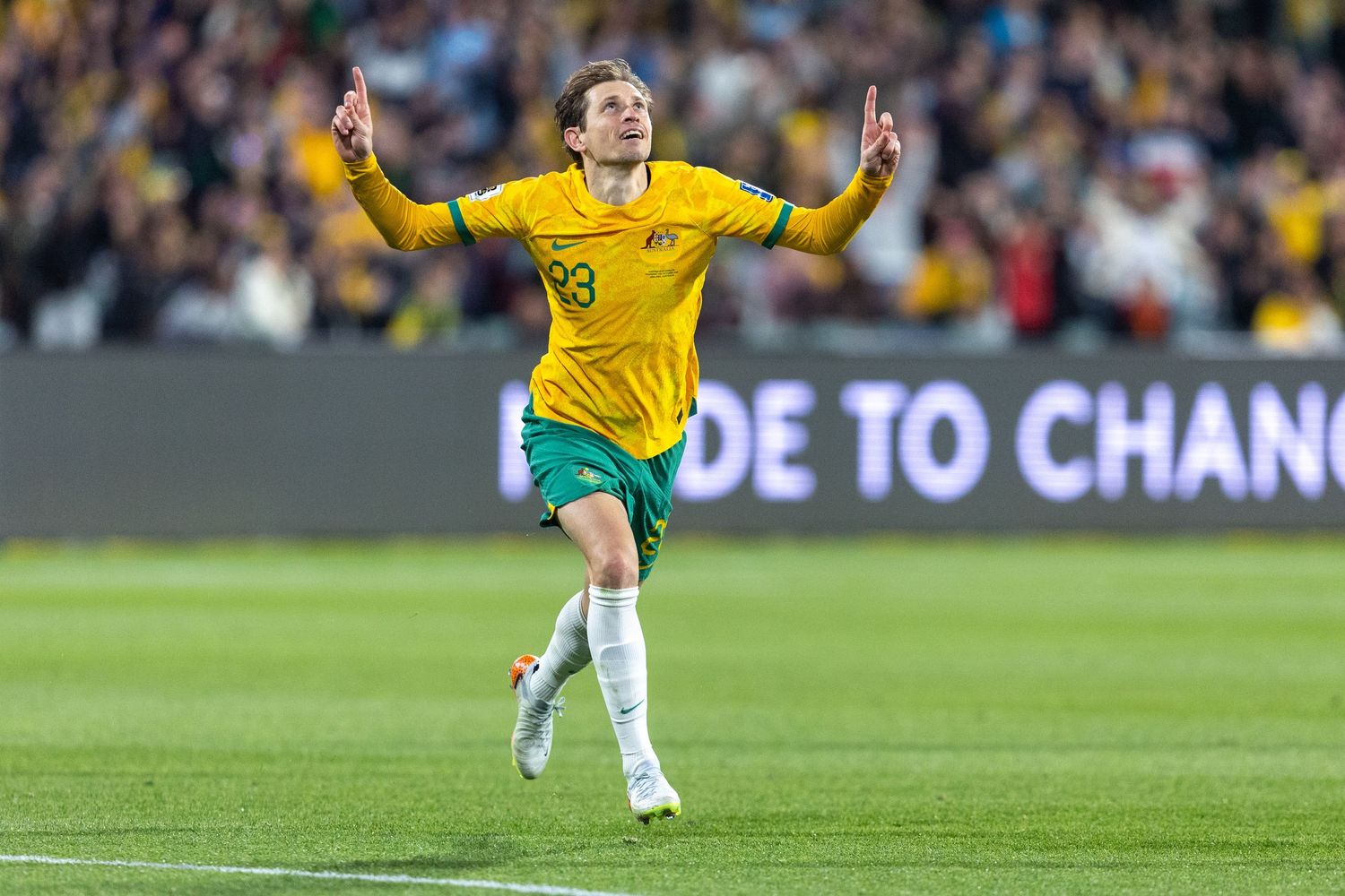 Soccer player in yellow Brazil jersey celebrates with arms raised during match.