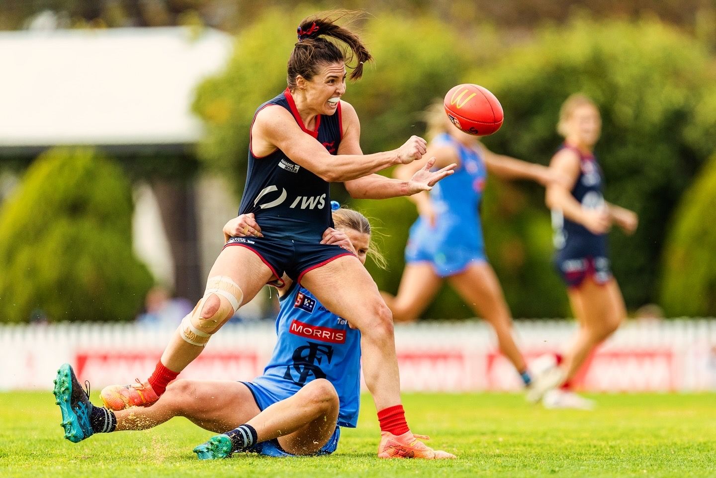 Women's football players compete for ball during match on grass field.