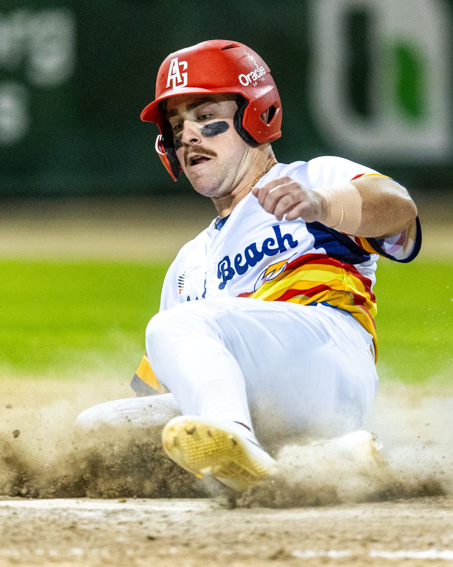 Baseball player slides dramatically into base creating a cloud of dirt.