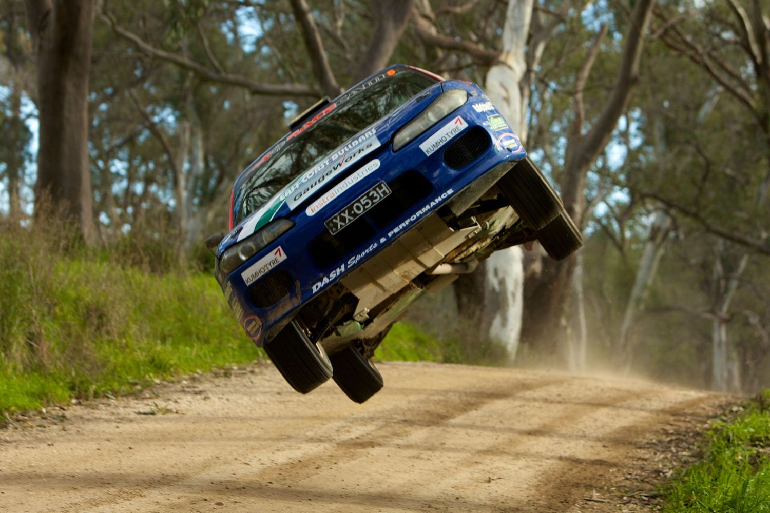 Off-road vehicle kicking up dust while driving through a rugged forest trail.