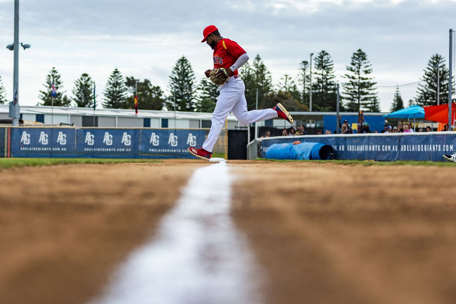 Baseball player runs along baseline during game with trees in background.