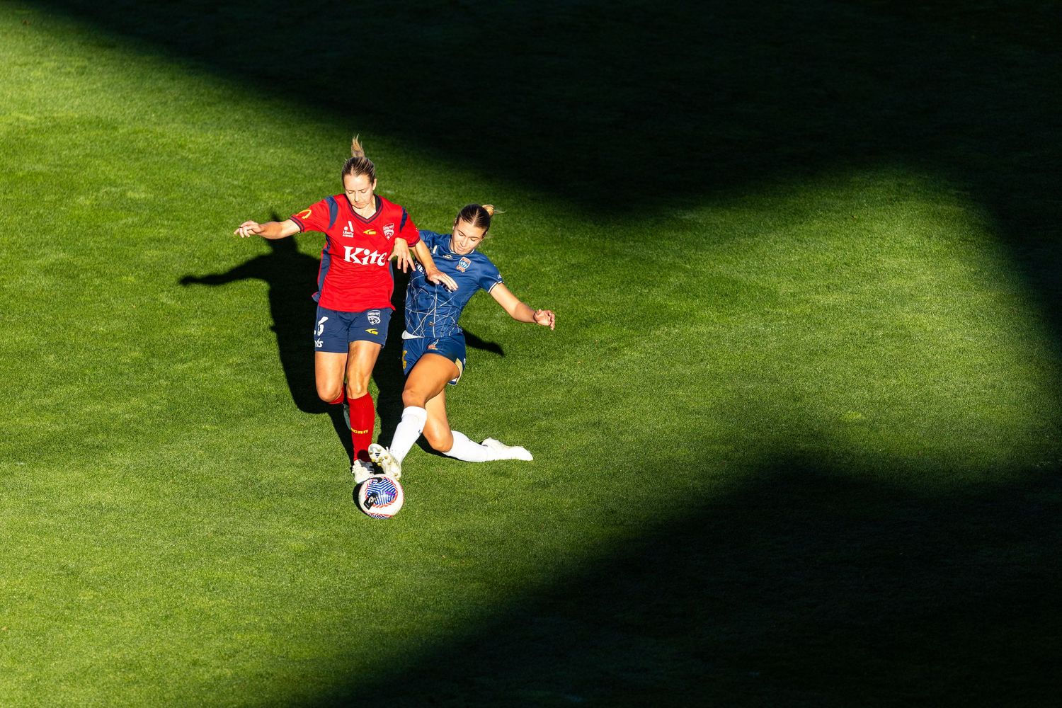 Athletes competing on a bright green sports field with dramatic lighting and shadows.