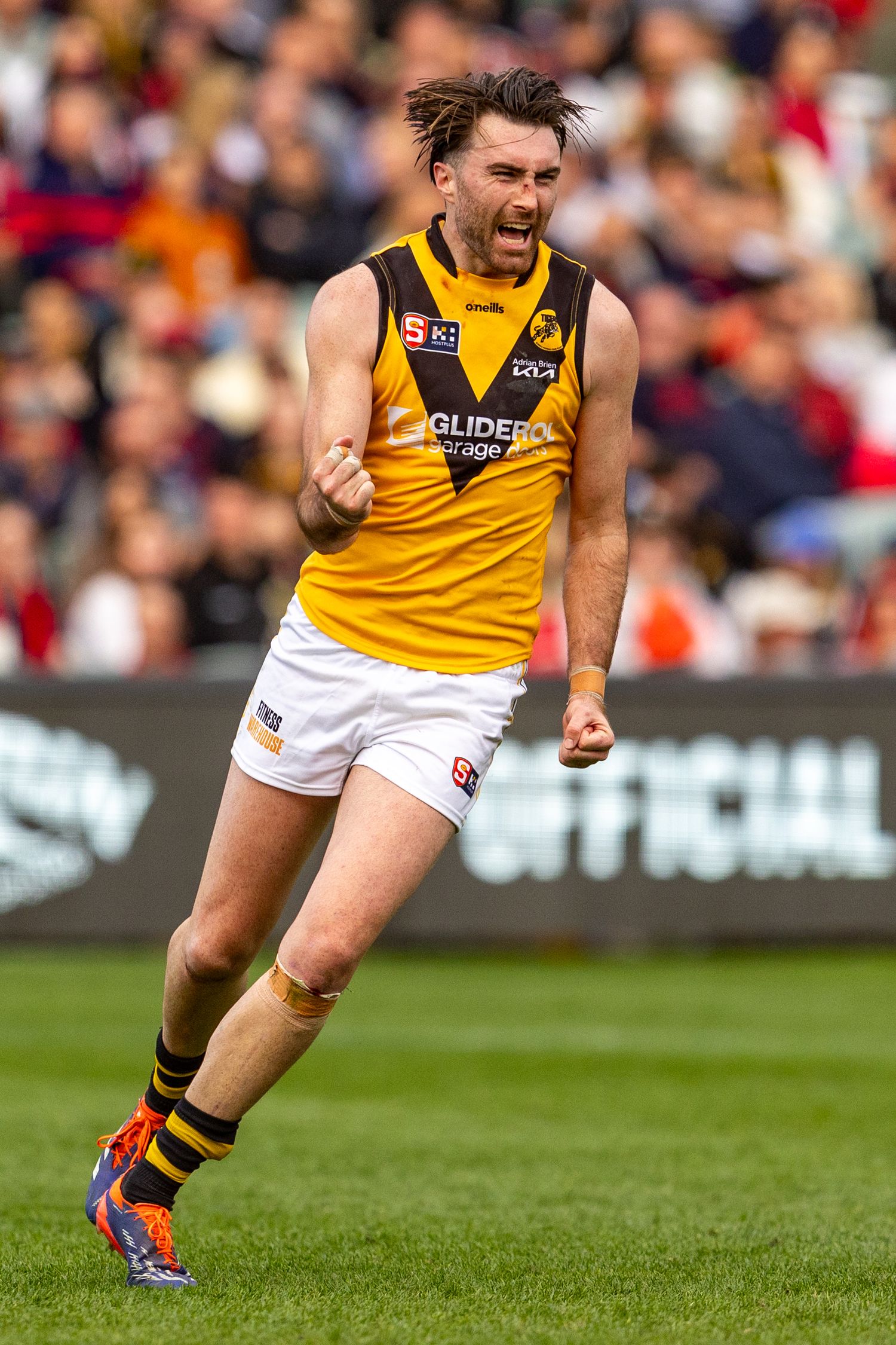Players in yellow and red uniforms running on grass during an Australian Rules Football match.