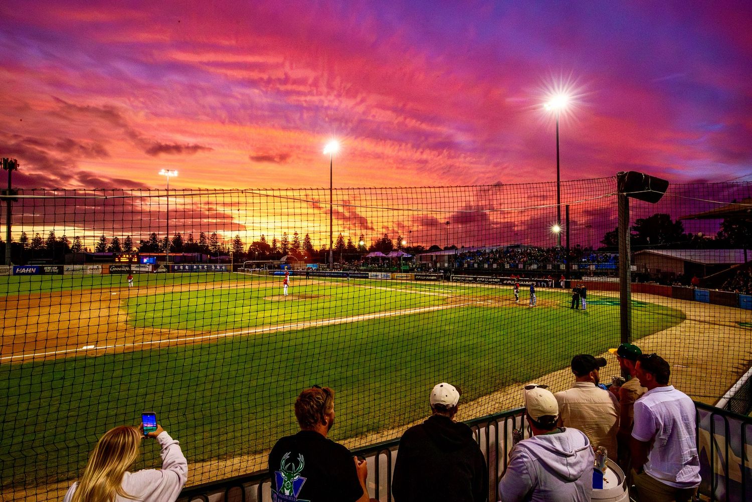 Stunning purple and orange sunset over baseball field with dramatic sky.