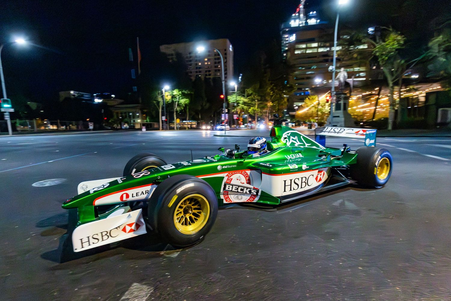Vintage Formula One race cars displayed at night under bright stadium lights on a city street.