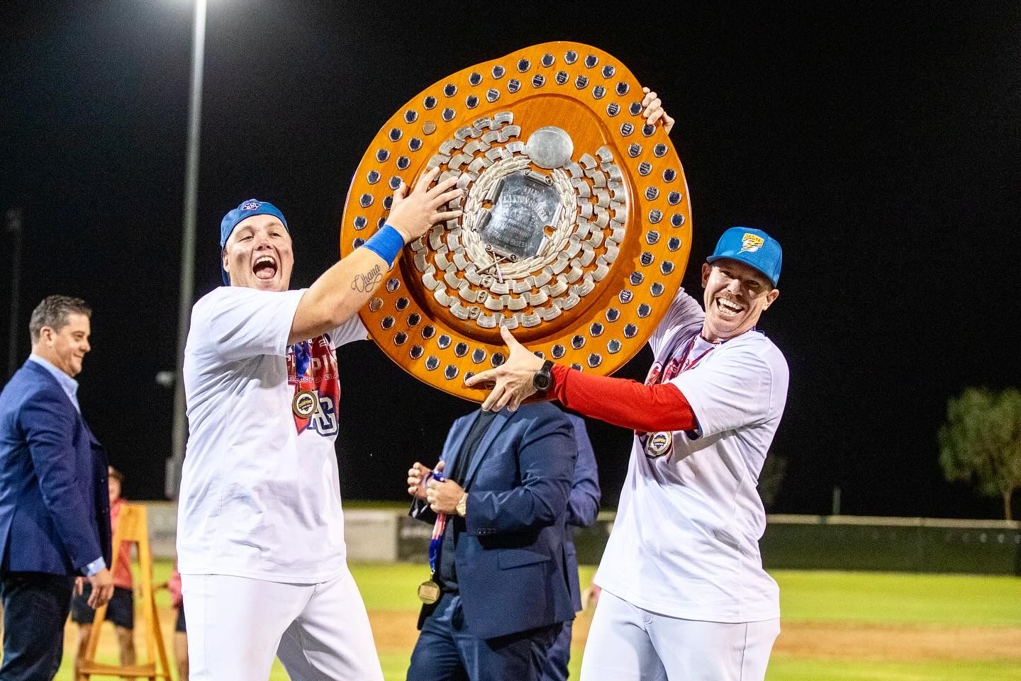 Players celebrate with large trophy under stadium lights at night.