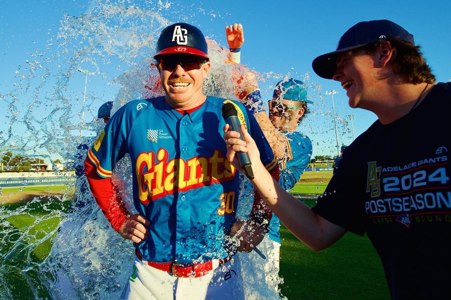 Baseball players spray water in celebration during outdoor game.