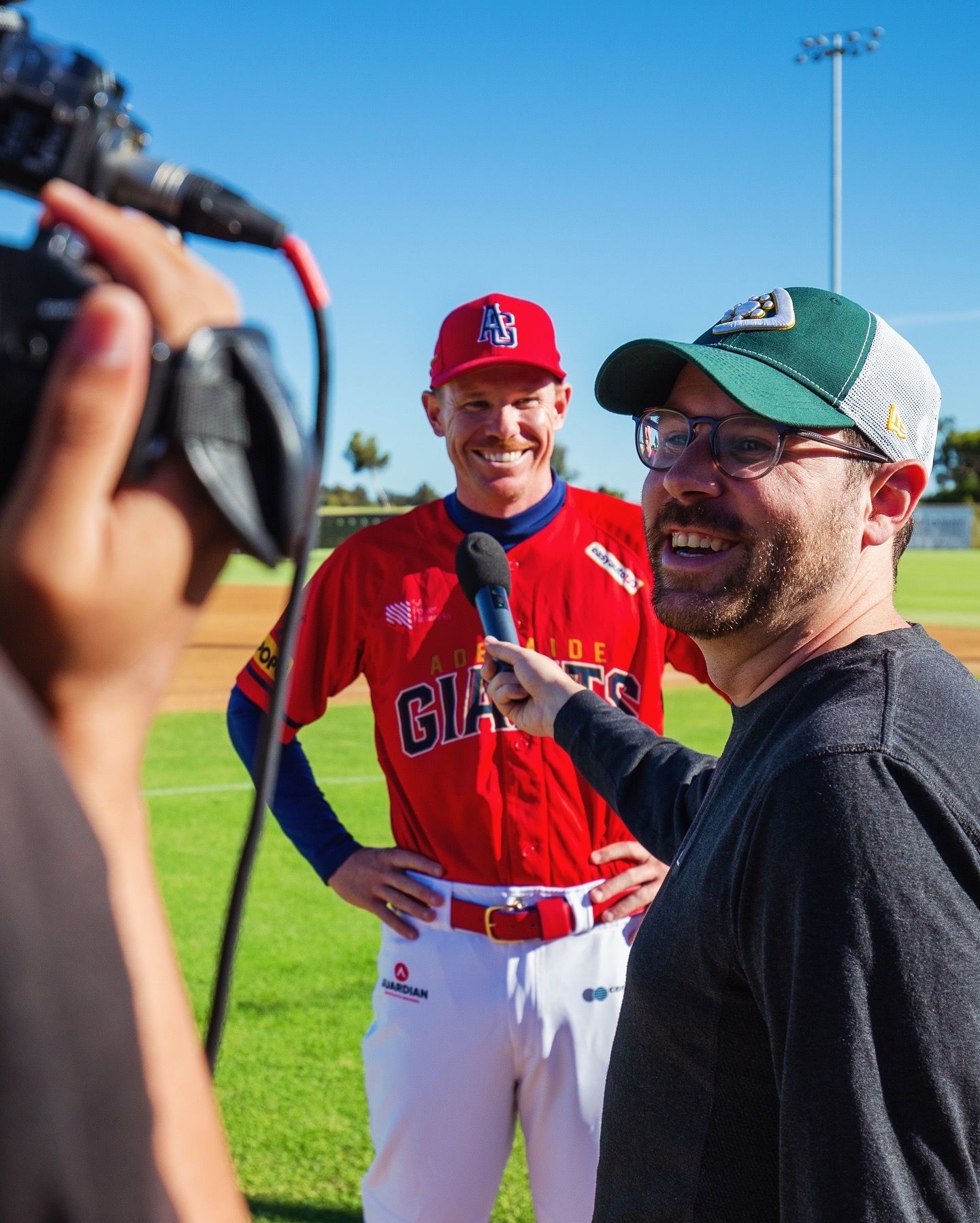 Baseball players and coaches gather on a sunny field during practice.