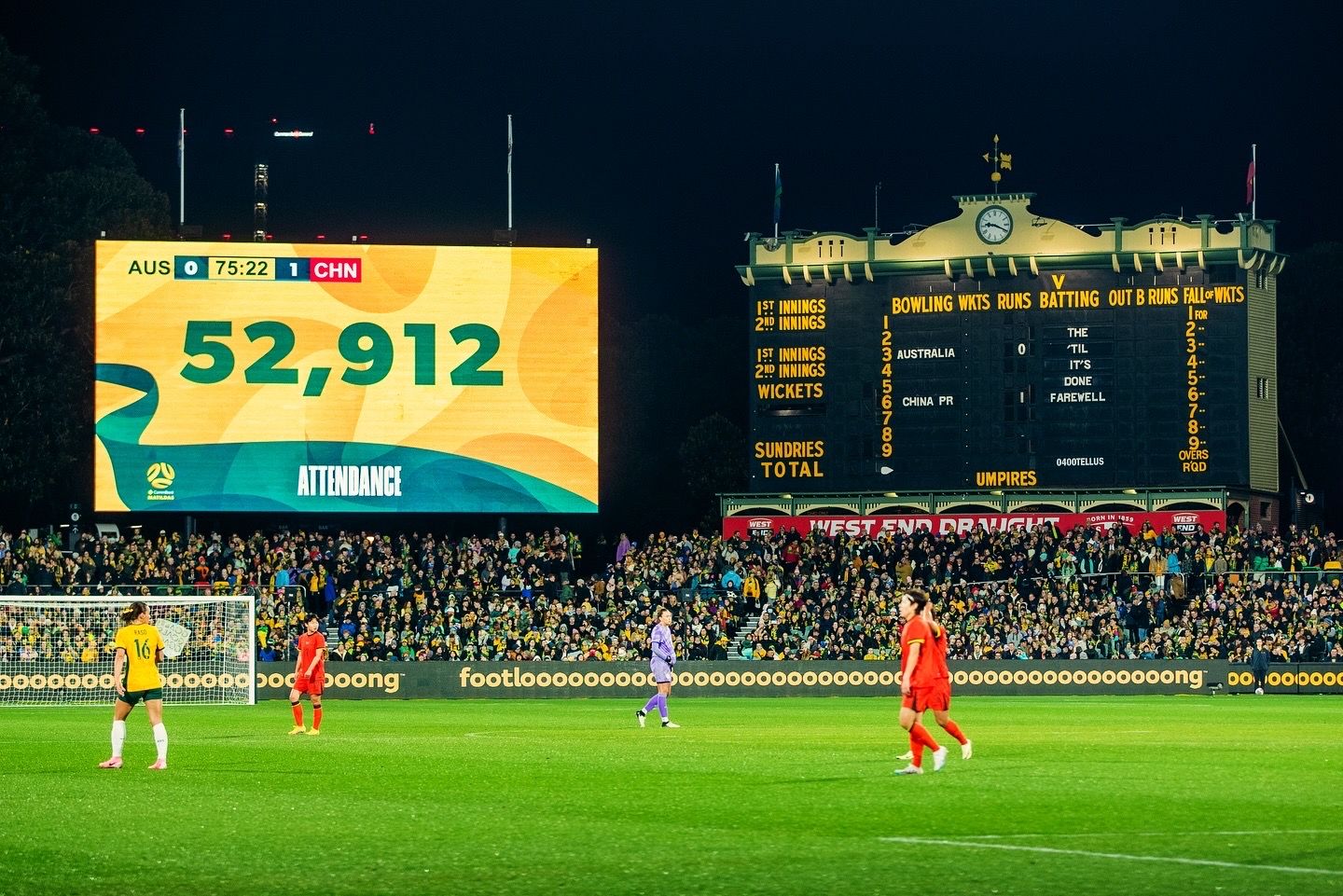 Night soccer match with illuminated scoreboard and stadium lights.