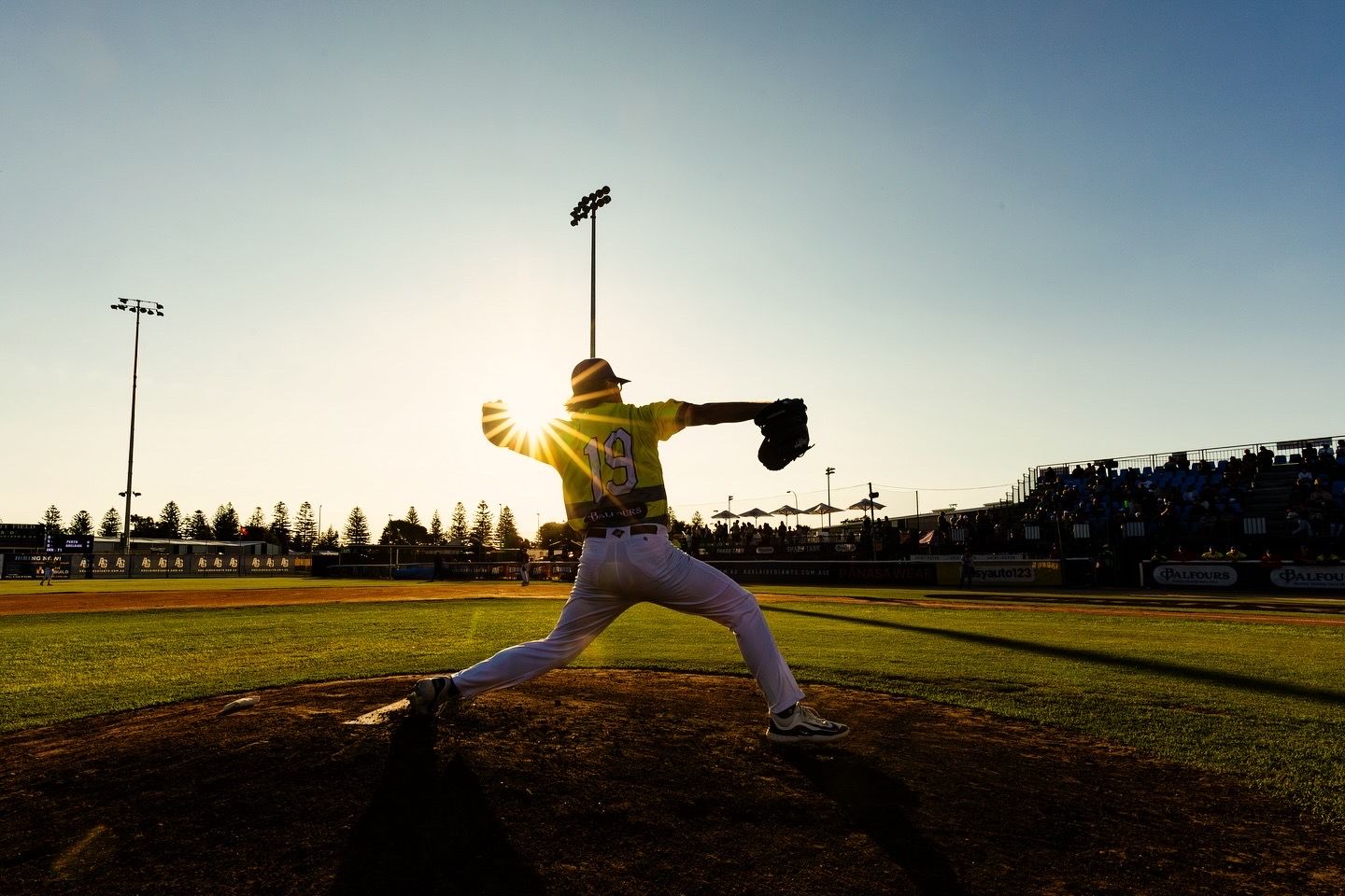 Baseball pitcher silhouetted against sunset throws pitch during game.