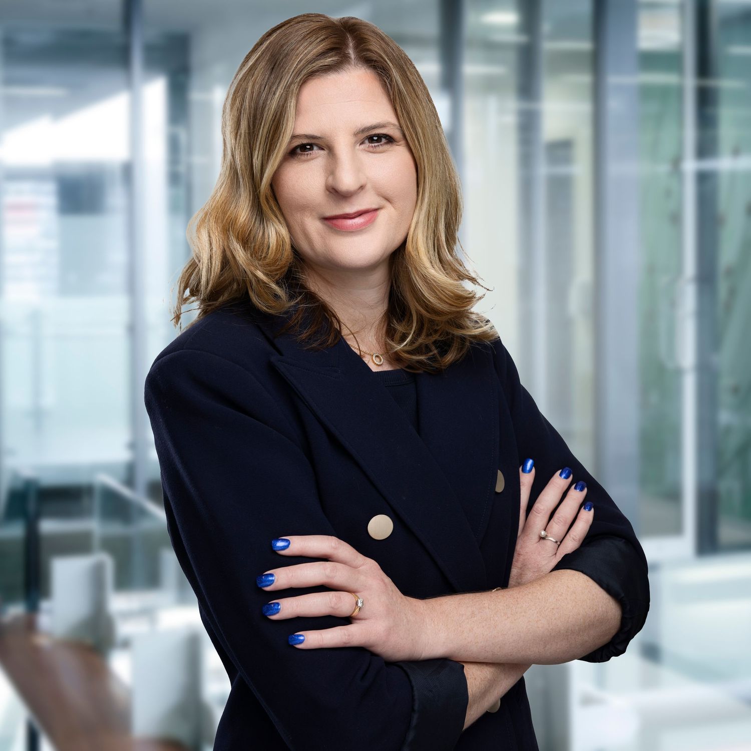 Business professional in black blazer poses confidently in modern office setting.