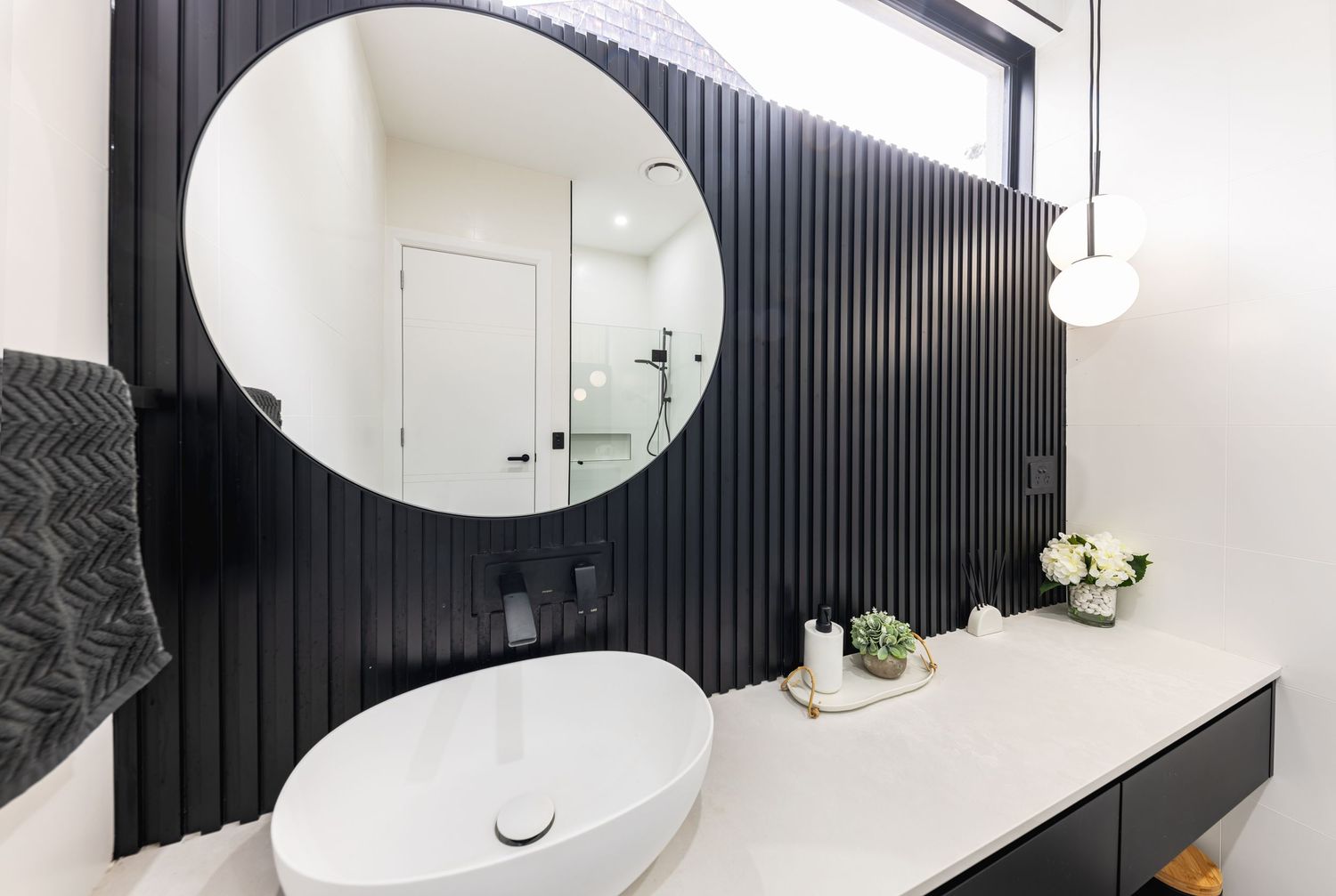 Modern bathroom interior with black vertical slat accent wall, round mirror, and white fixtures.