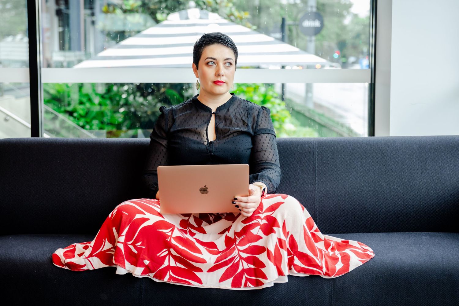 Professional in casual attire lounges on black couch with laptop in modern setting.