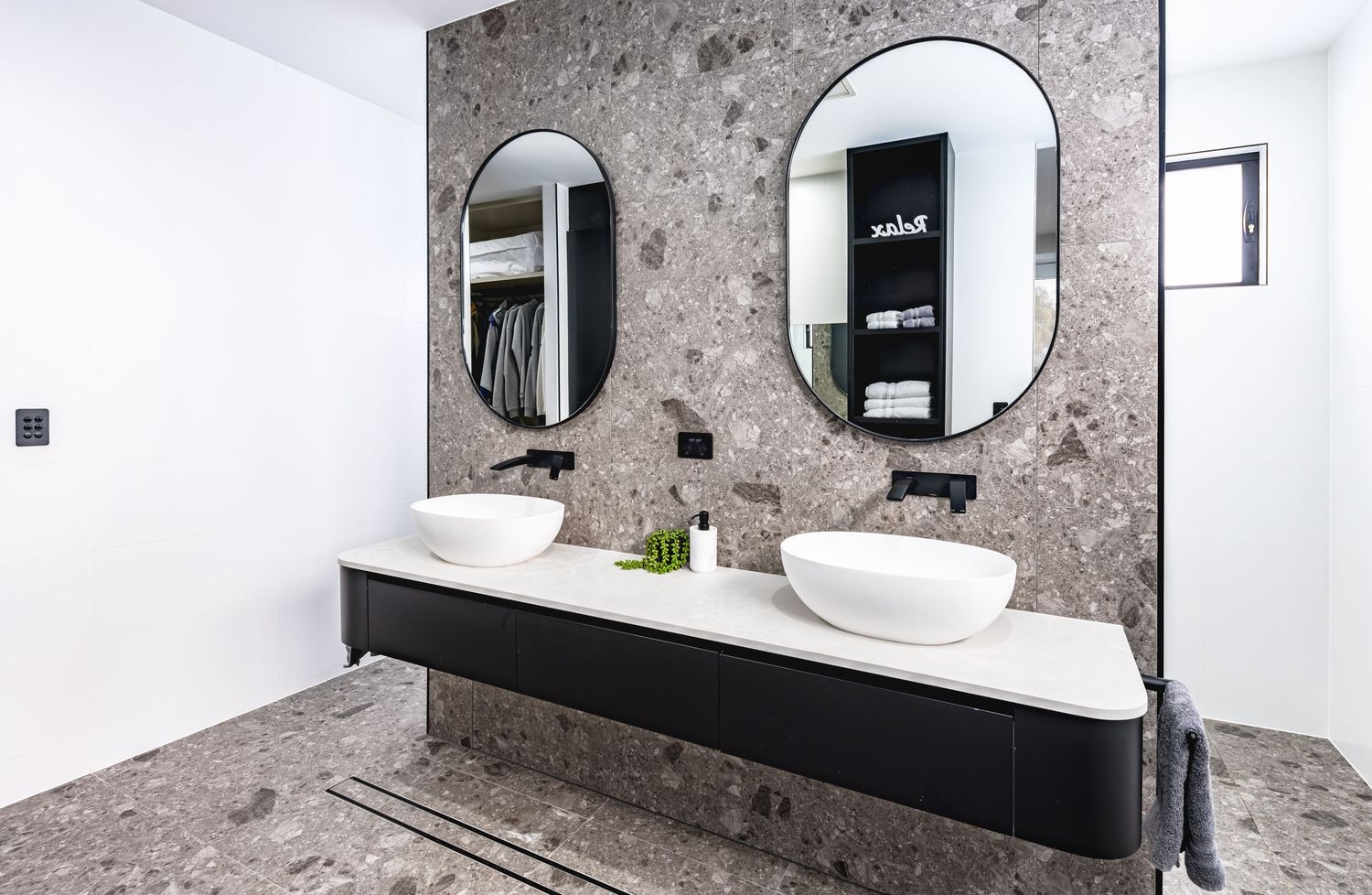 Modern bathroom interior with dual vessel sinks, oval mirrors, and marble-patterned wall featuring black floating vanity.
