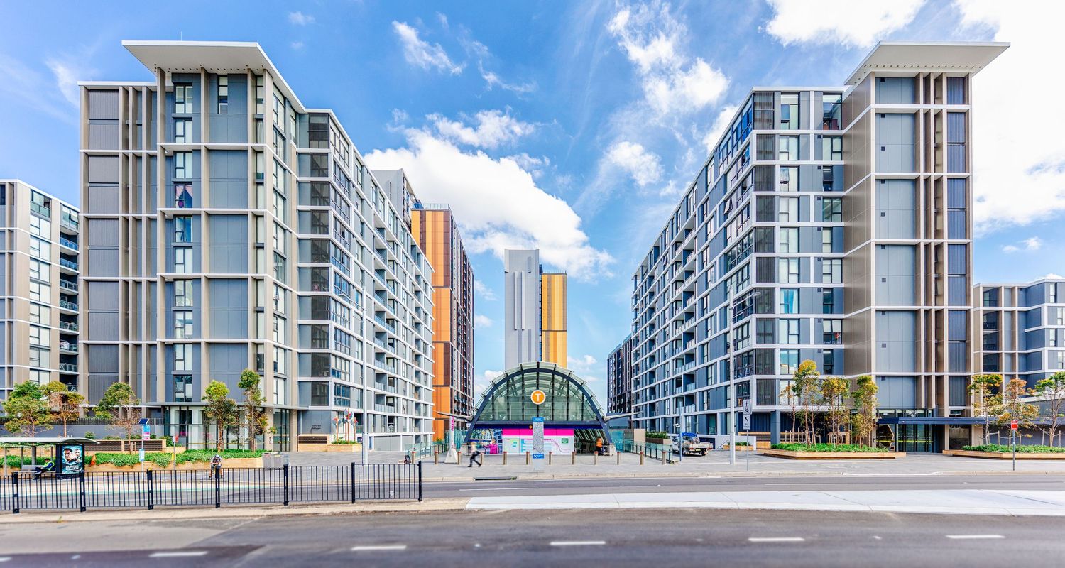 Panoramic view of modern residential apartment buildings with glass balconies against a bright blue sky.