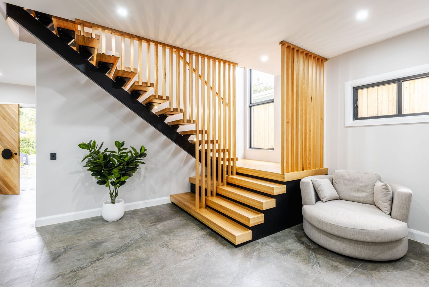 Modern basement renovation with wooden staircase, recessed lighting, and polished concrete floors in a minimalist design.