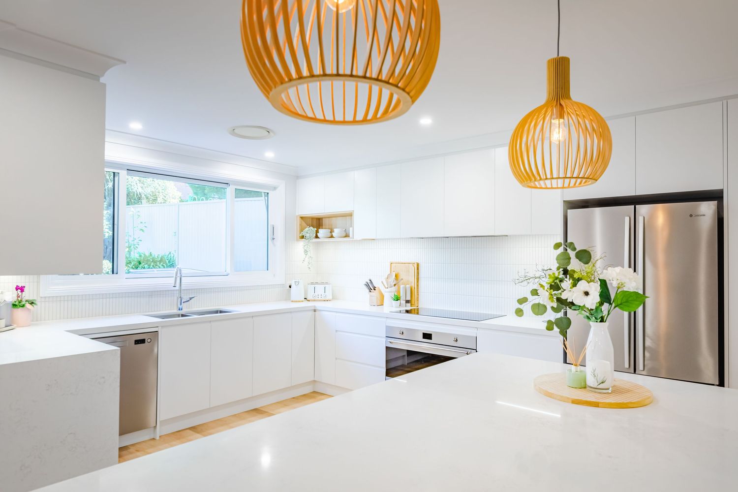 Modern white kitchen with orange pendant lights features sleek cabinetry and a minimalist design aesthetic.