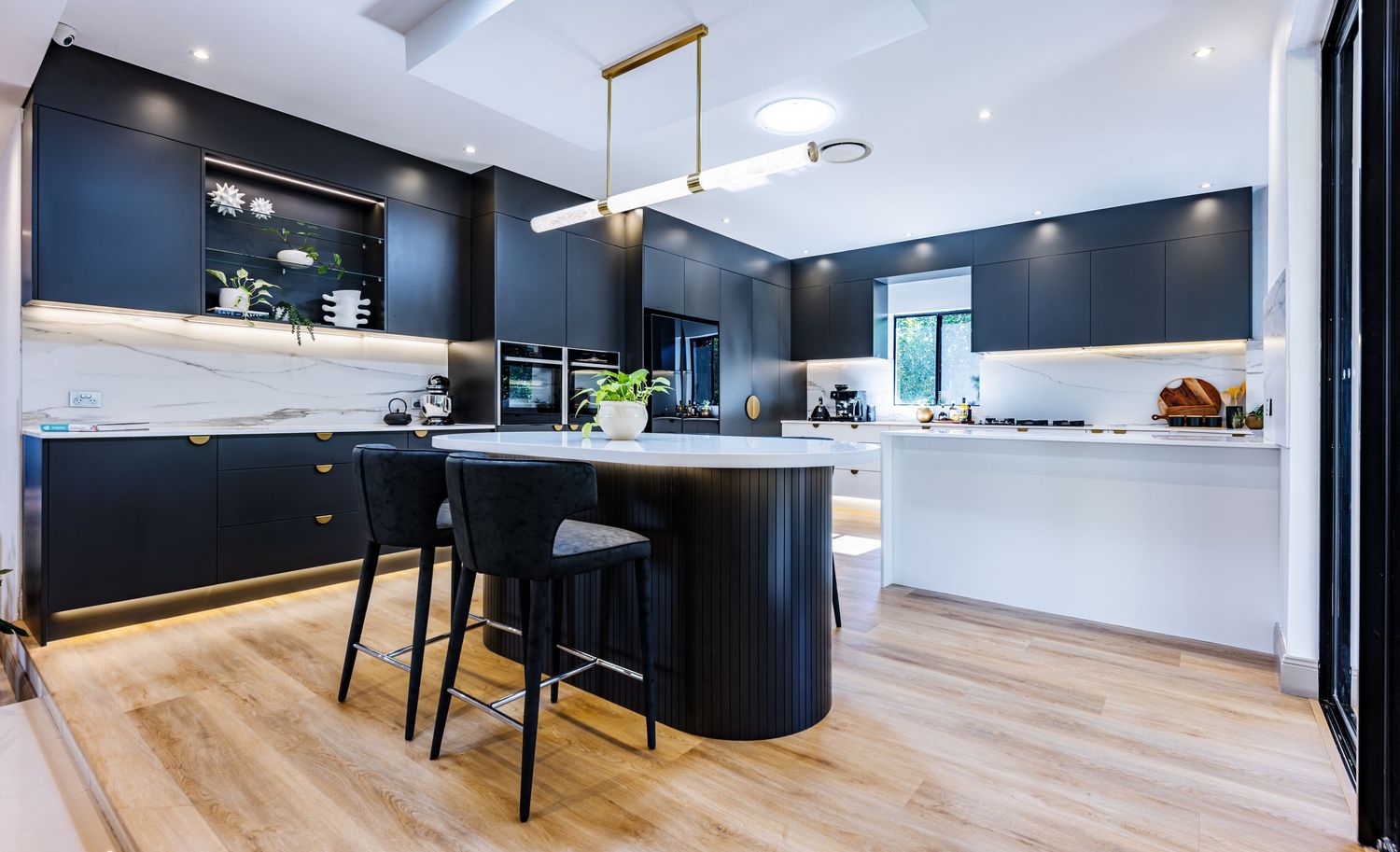 Modern kitchen interior with matte black cabinets, light wood flooring, and curved island with bar seating.