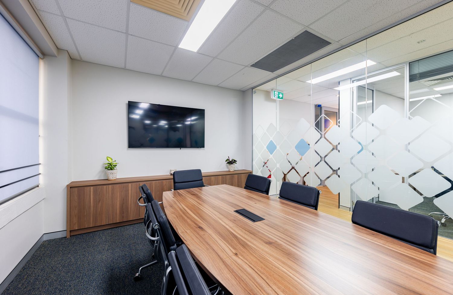 Modern office meeting room with wooden conference table, black chairs, and geometric wall patterns in panoramic view.