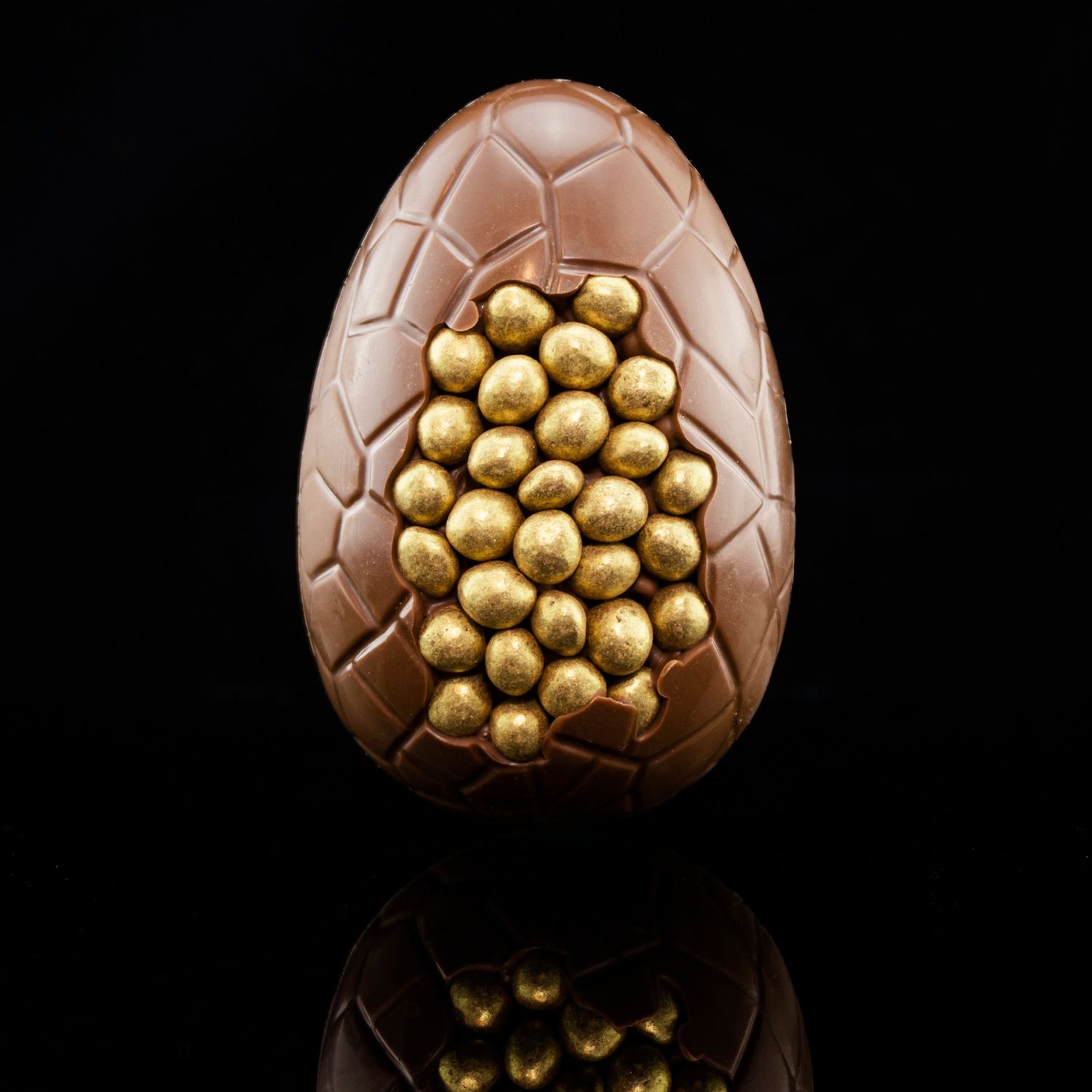 Luxury chocolate Easter egg with gold decorative balls against black background.