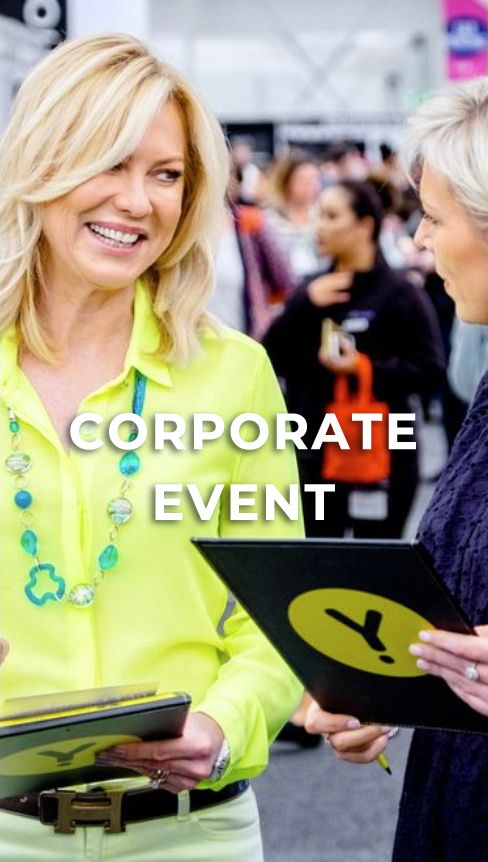 Corporate event attendee in bright yellow shirt holds tablet device while networking with others at business gathering.
