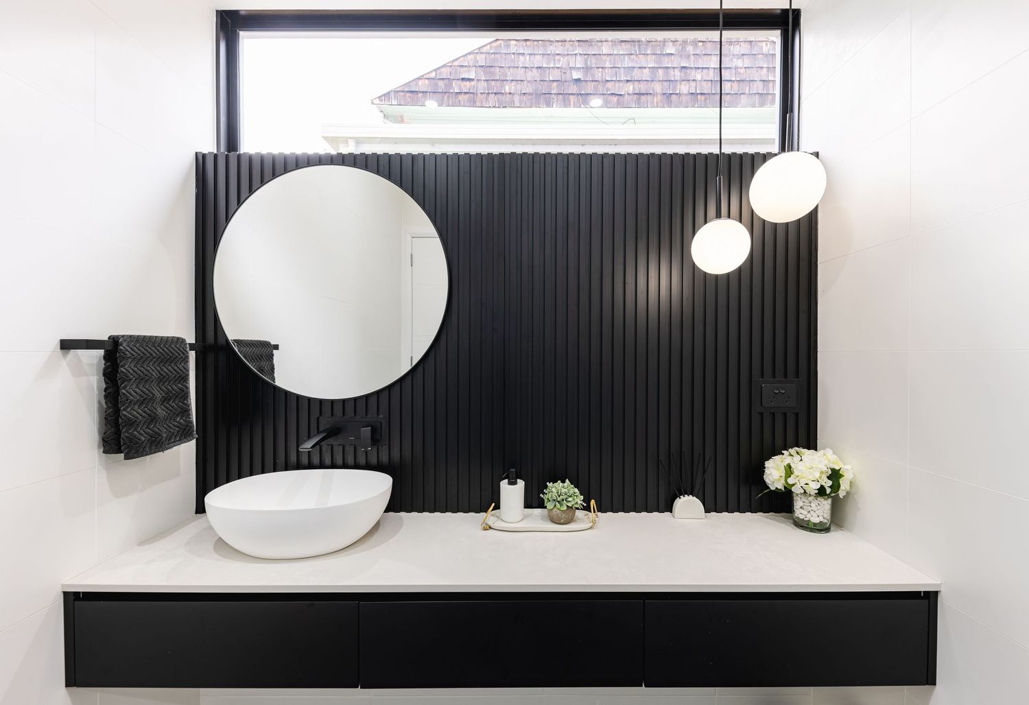 A modern bathroom interior features black wall panels, round mirrors, and white pendant lights creating a sleek design.