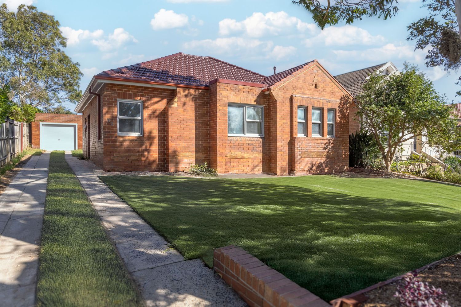 Panoramic view of a brick house with red tile roof and well-maintained green lawn on a sunny day.