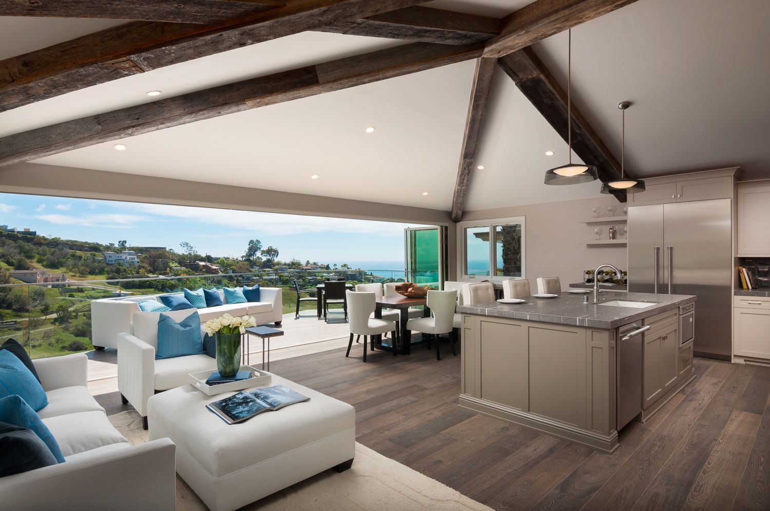 Modern open concept living room and kitchen with panoramic ocean views, white furniture and hardwood floors.