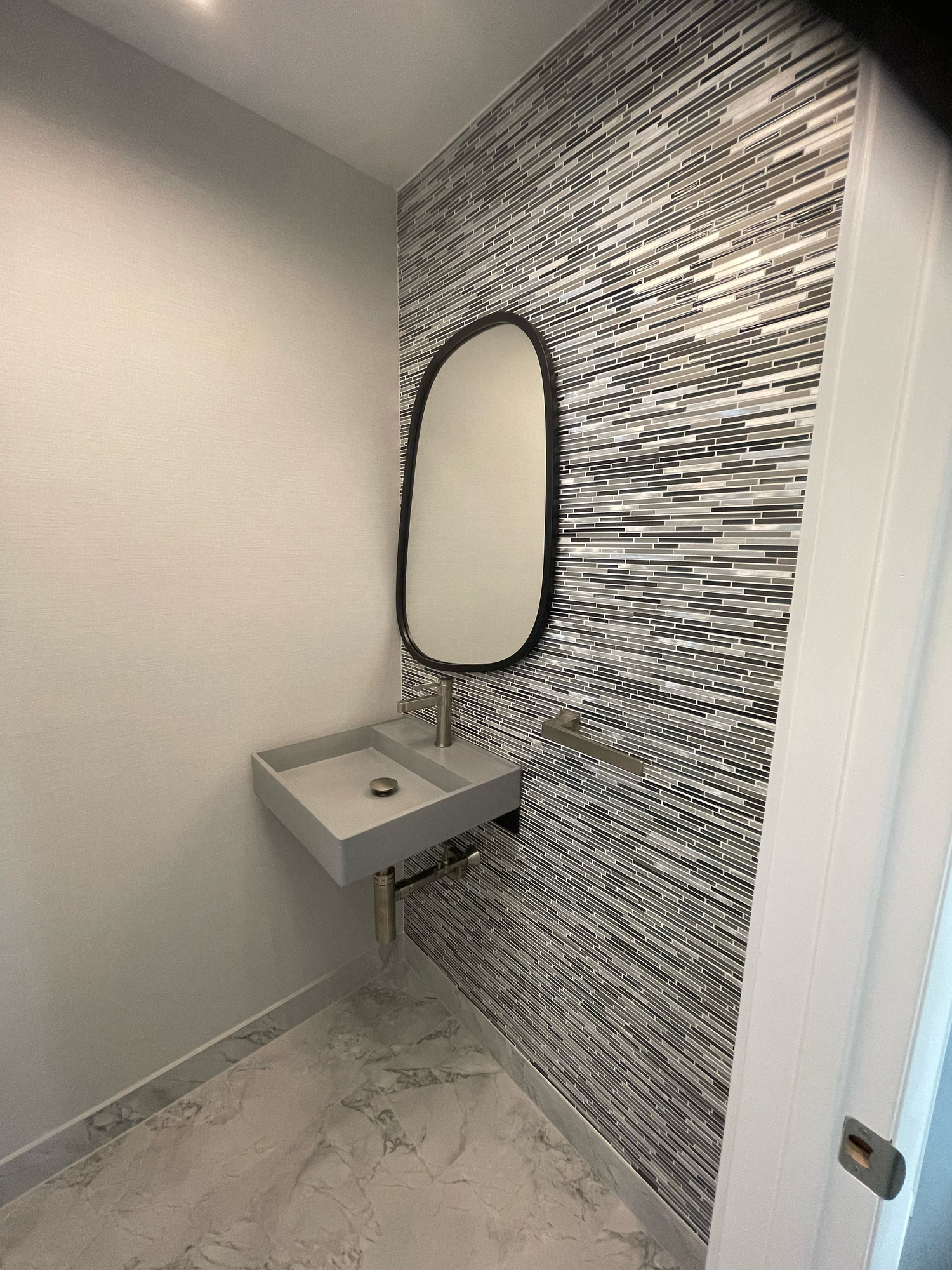 Modern bathroom wall features sleek gray mosaic tile accent with white walls and contemporary lighting fixtures.