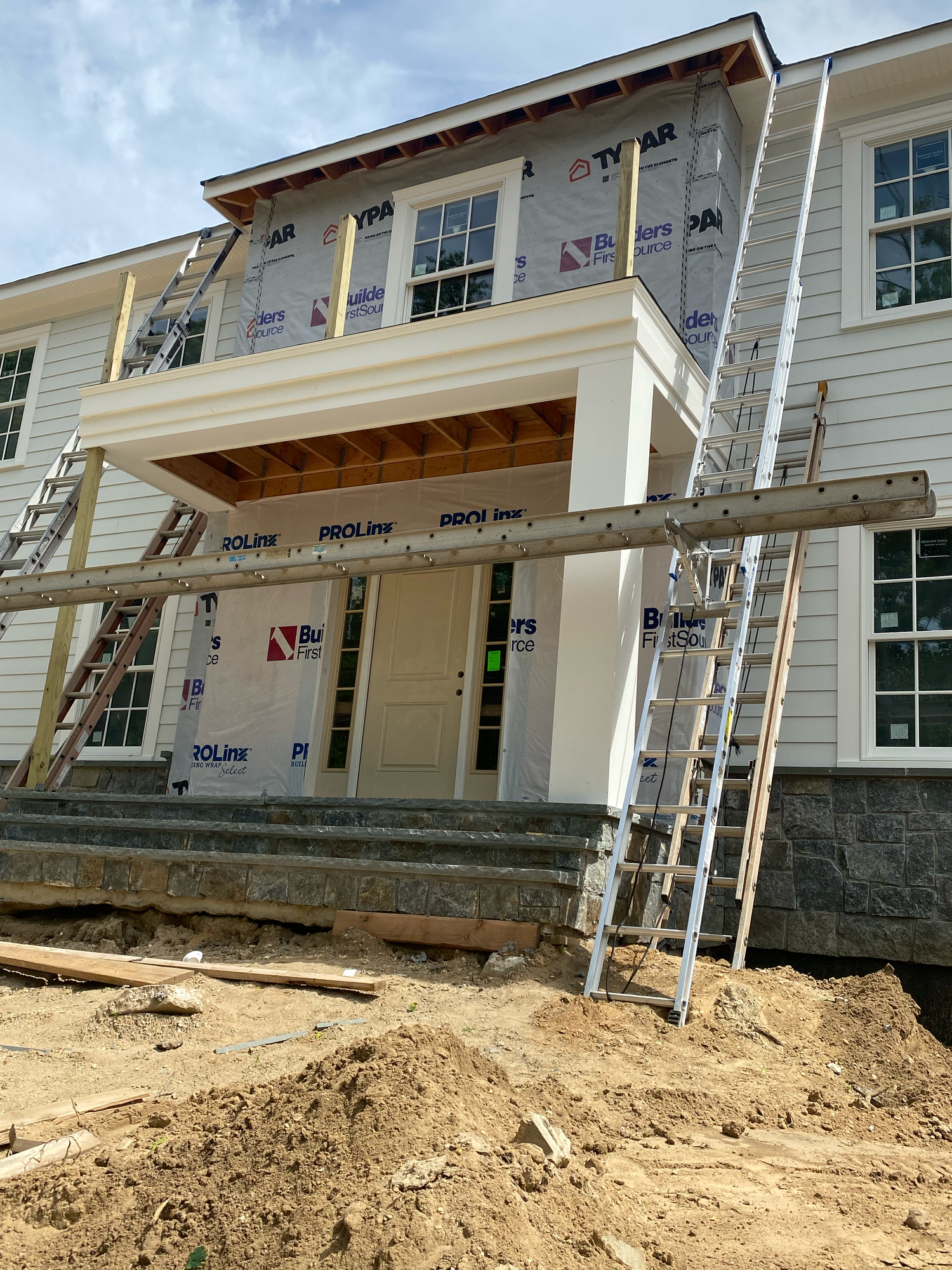 Construction progress shows exterior siding and windows installed on a new residential building with exposed foundation.