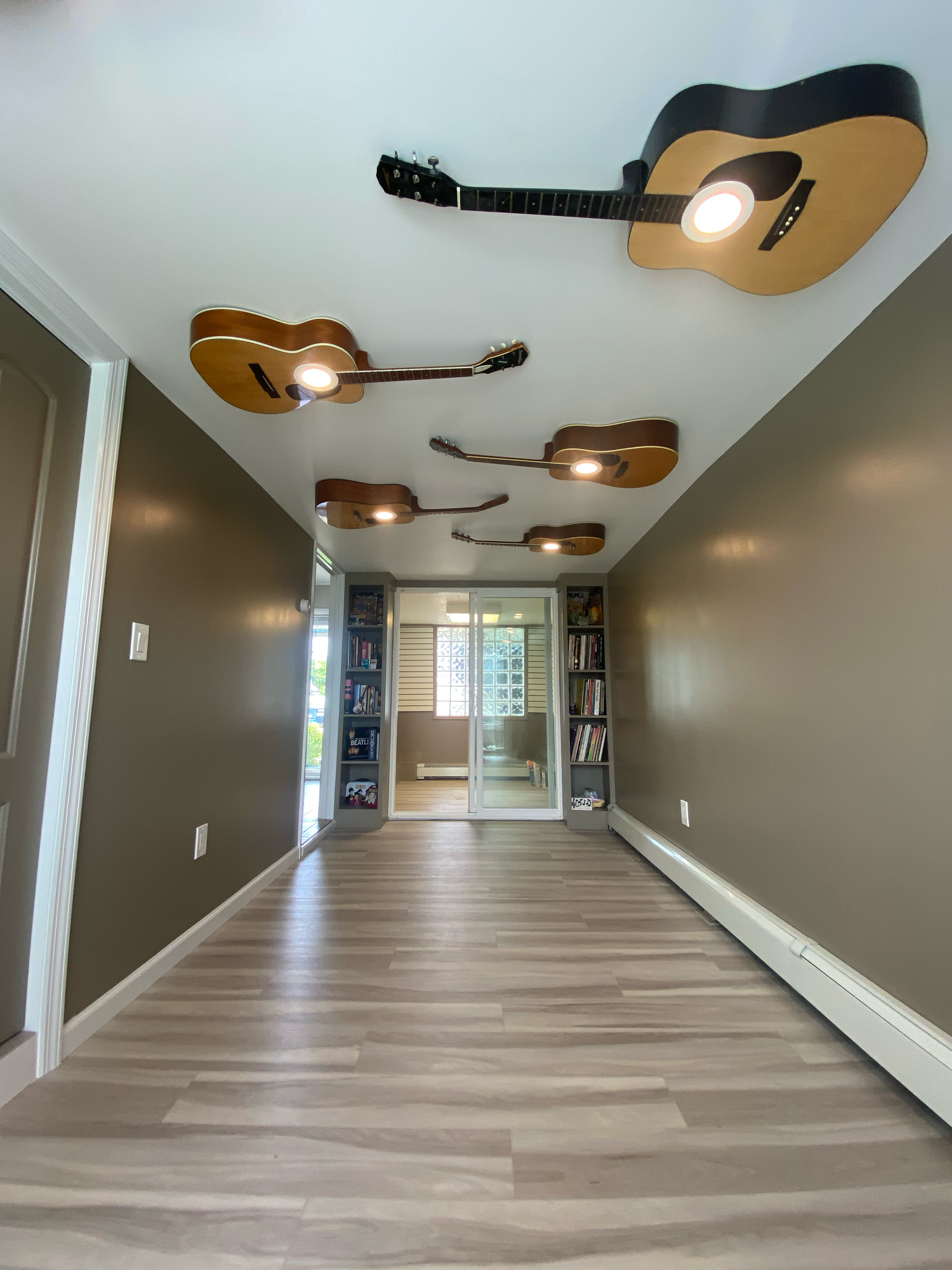 Acoustic guitars mounted as decorative light fixtures on a hallway ceiling create unique ambient lighting.