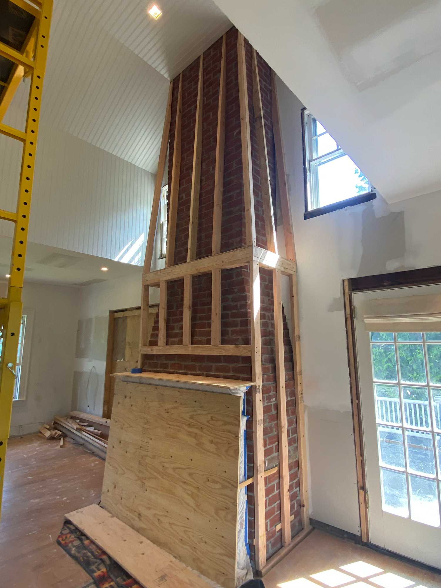 Interior construction view of a tall fireplace frame with exposed framing and a triangular window above in a vaulted ceiling room.