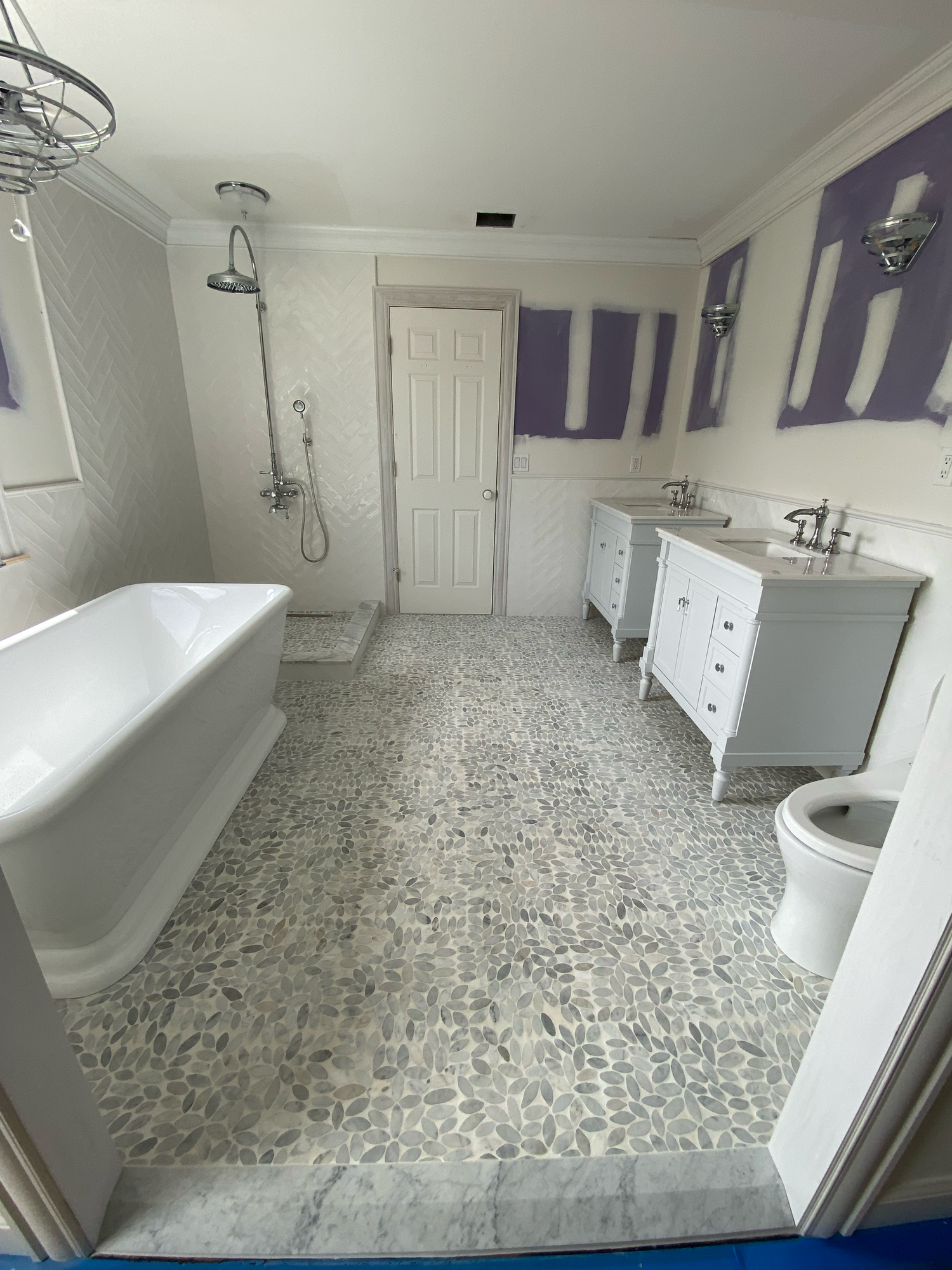 Modern white bathroom interior with pebble stone floor tiles, freestanding tub, and glass shower enclosure.