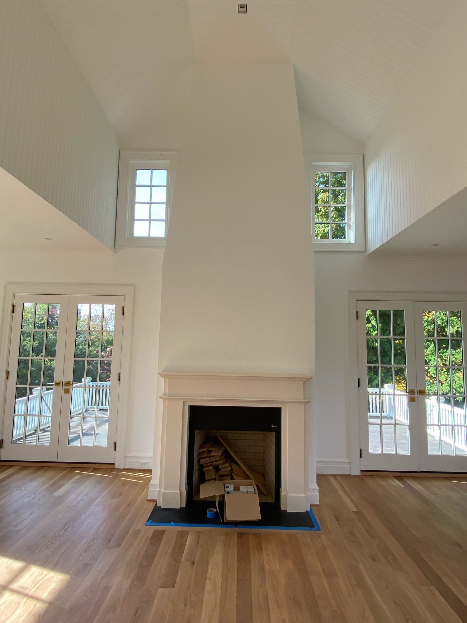 Interior room with vaulted ceilings, white walls, hardwood floors and multiple windows showing natural light streaming in.