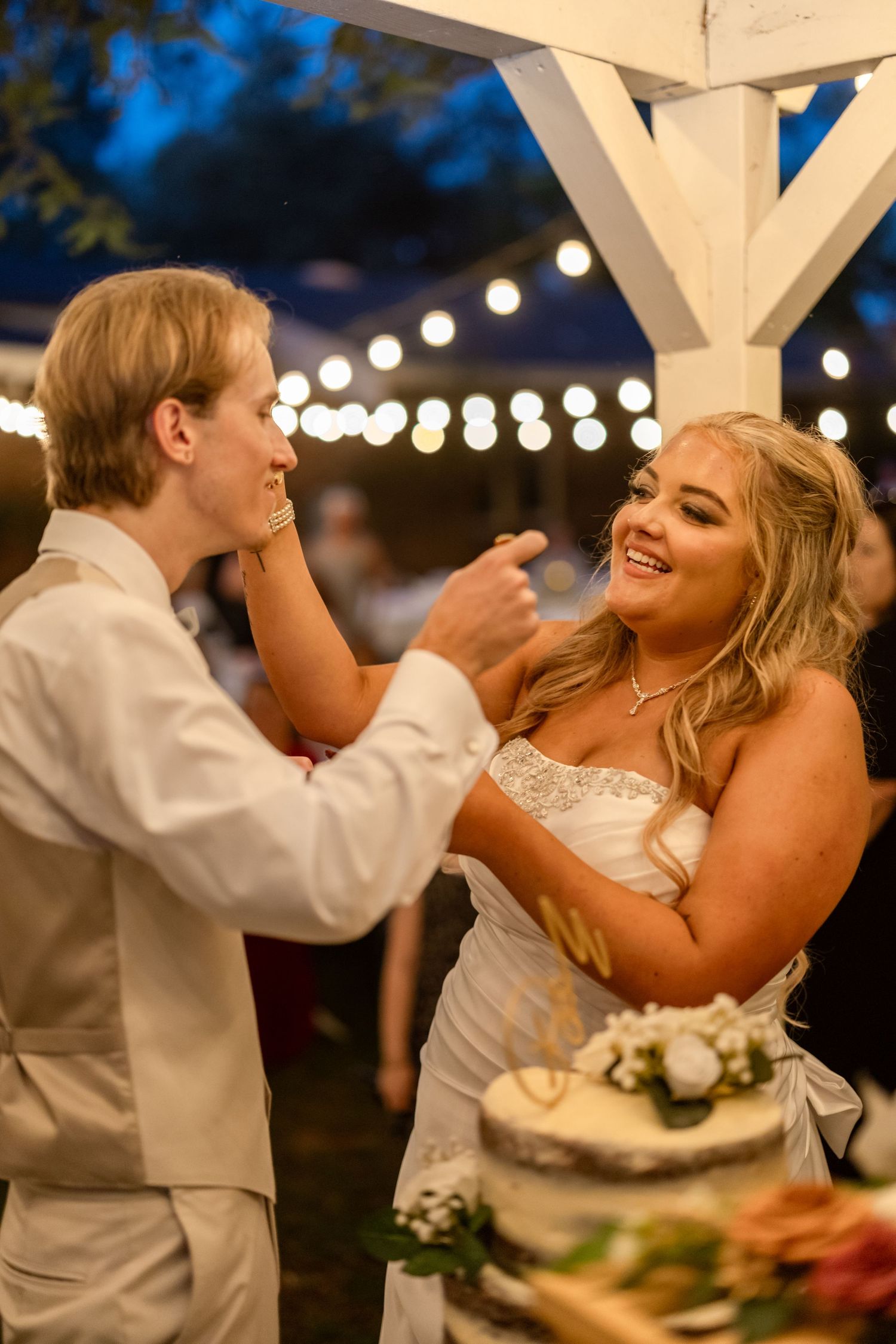Joyful couple sharing wedding cake and laughing during traditional cake-cutting moment.